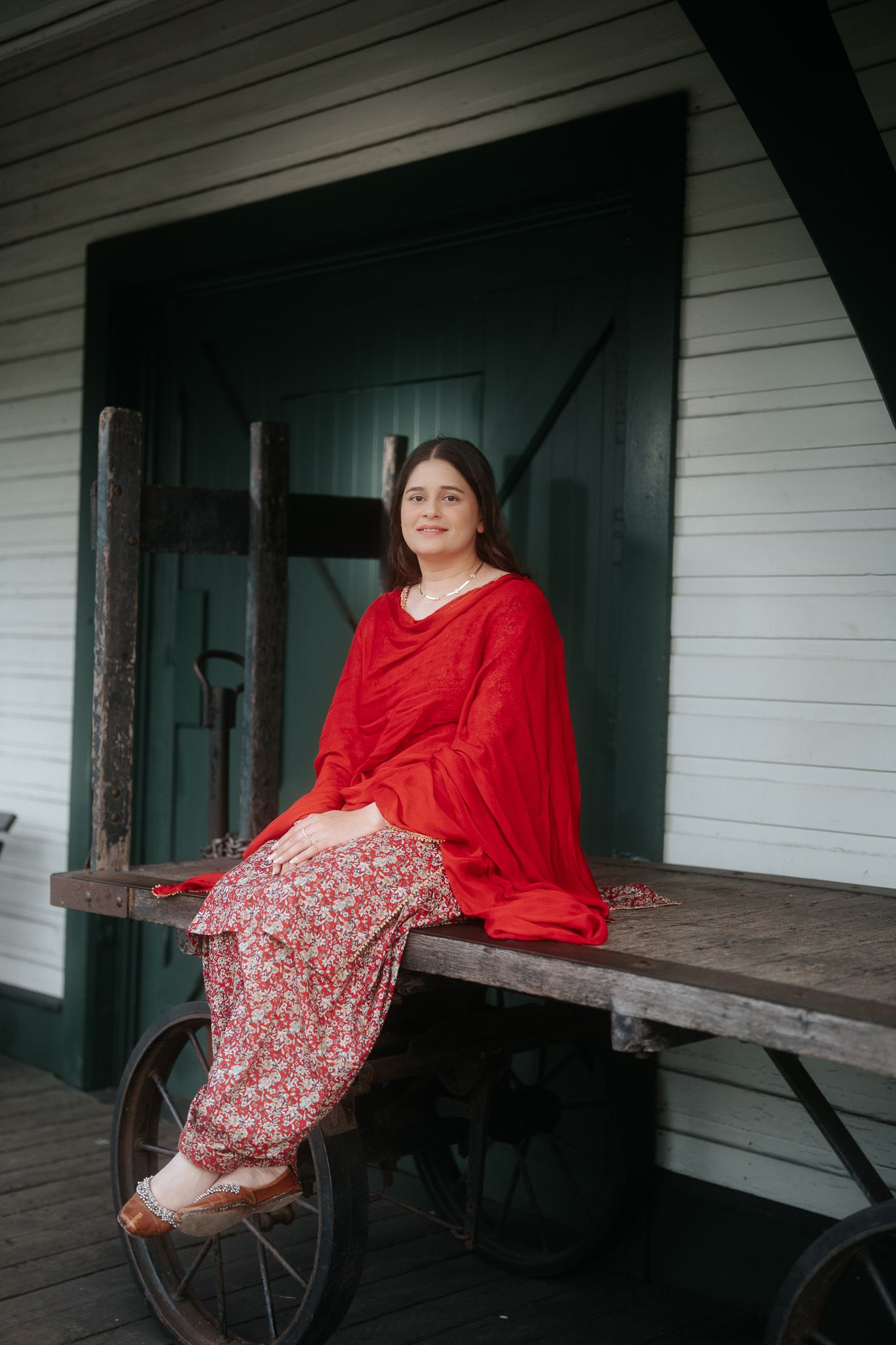 Woman in red salwar kameez sitting on vintage wooden cart outside historic building.