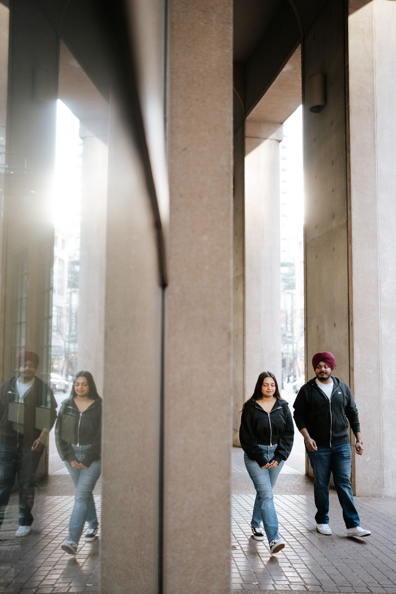 A sequence of architectural columns with people walking between them creates a rhythmic visual pattern in an urban setting.