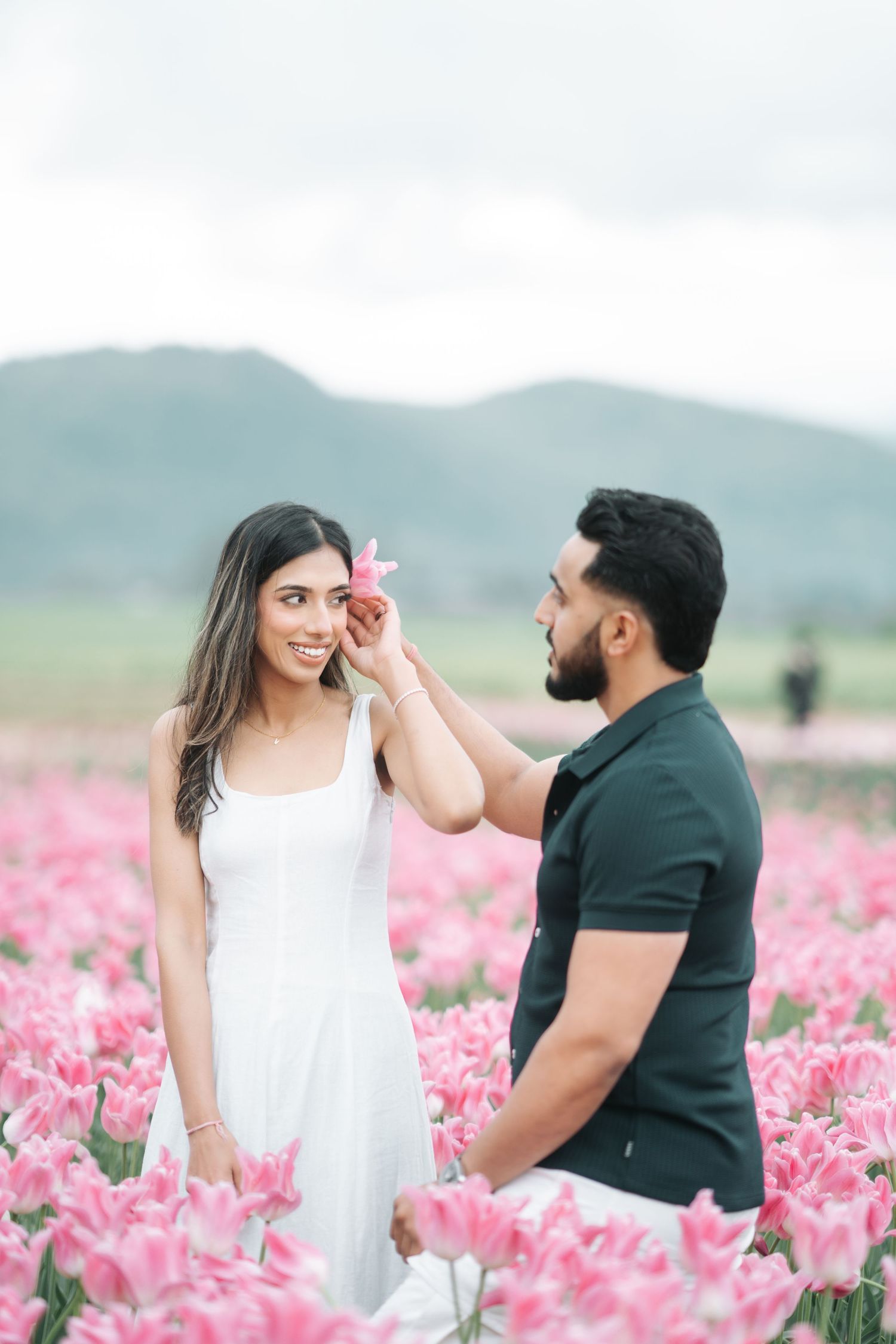 A couple shares a romantic moment in a vibrant pink tulip field with mountains in the background.
