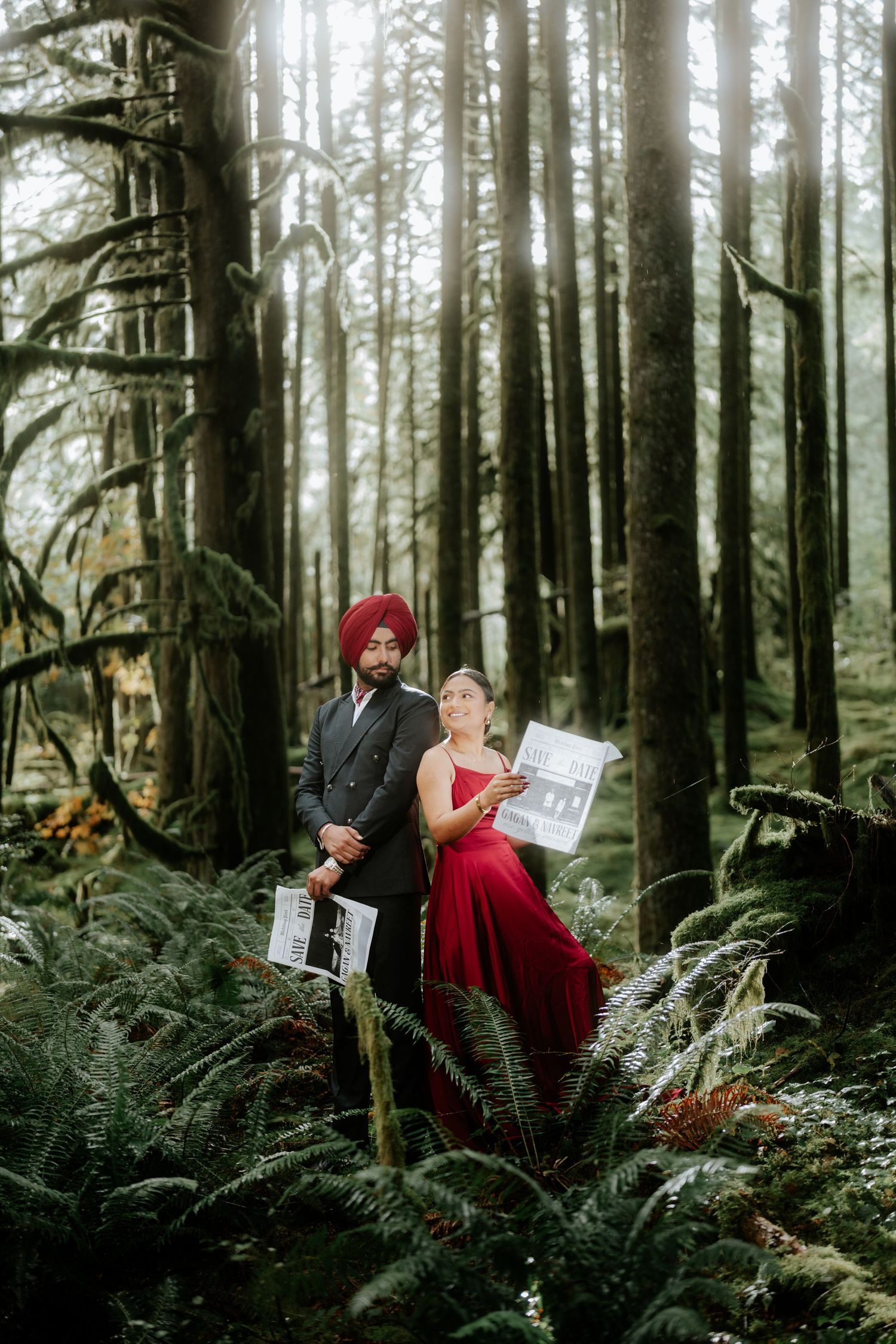 A romantic forest photoshoot featuring a couple holding newspapers amidst towering trees.