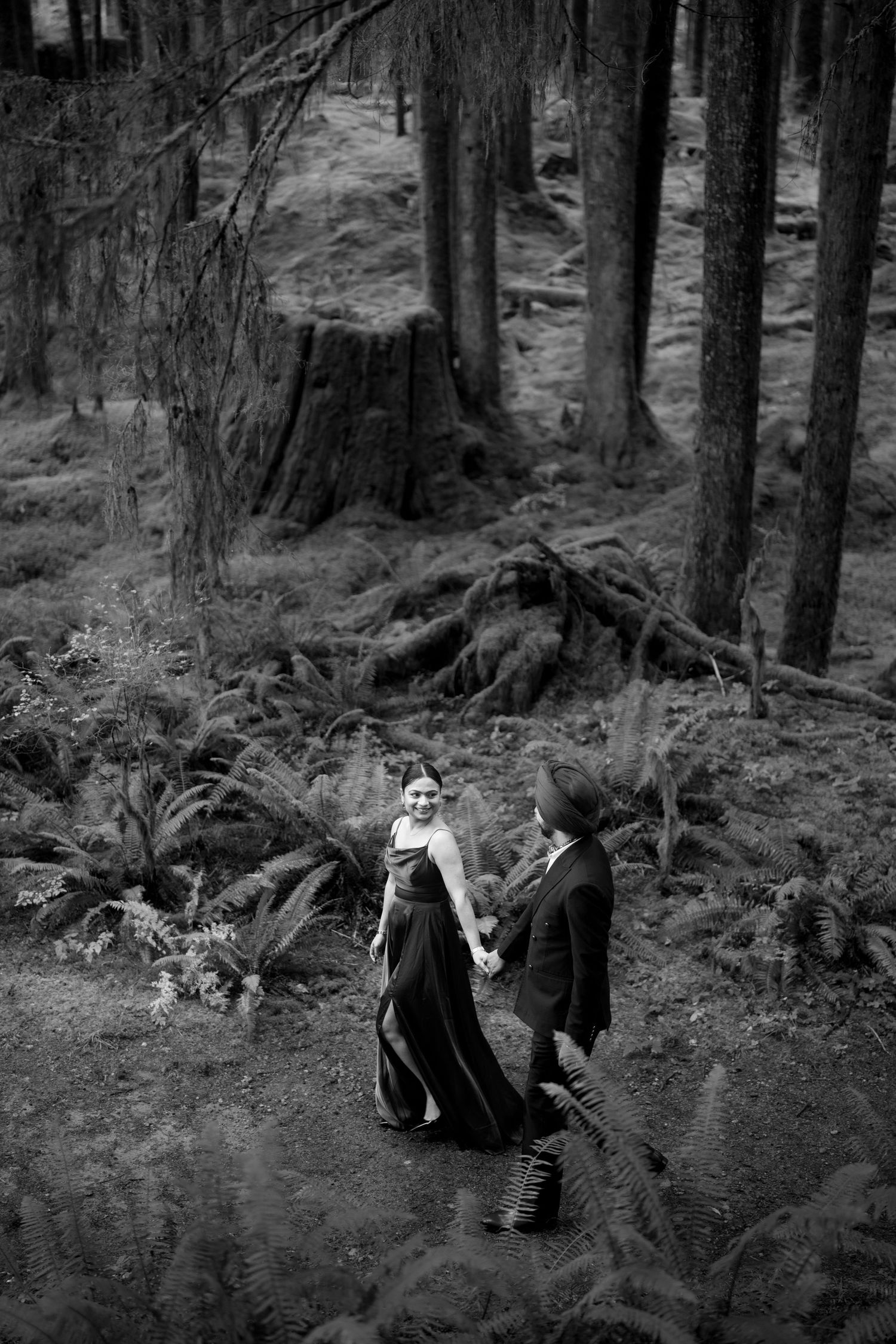 Black and white photo of two people walking along a forest trail surrounded by tall trees.
