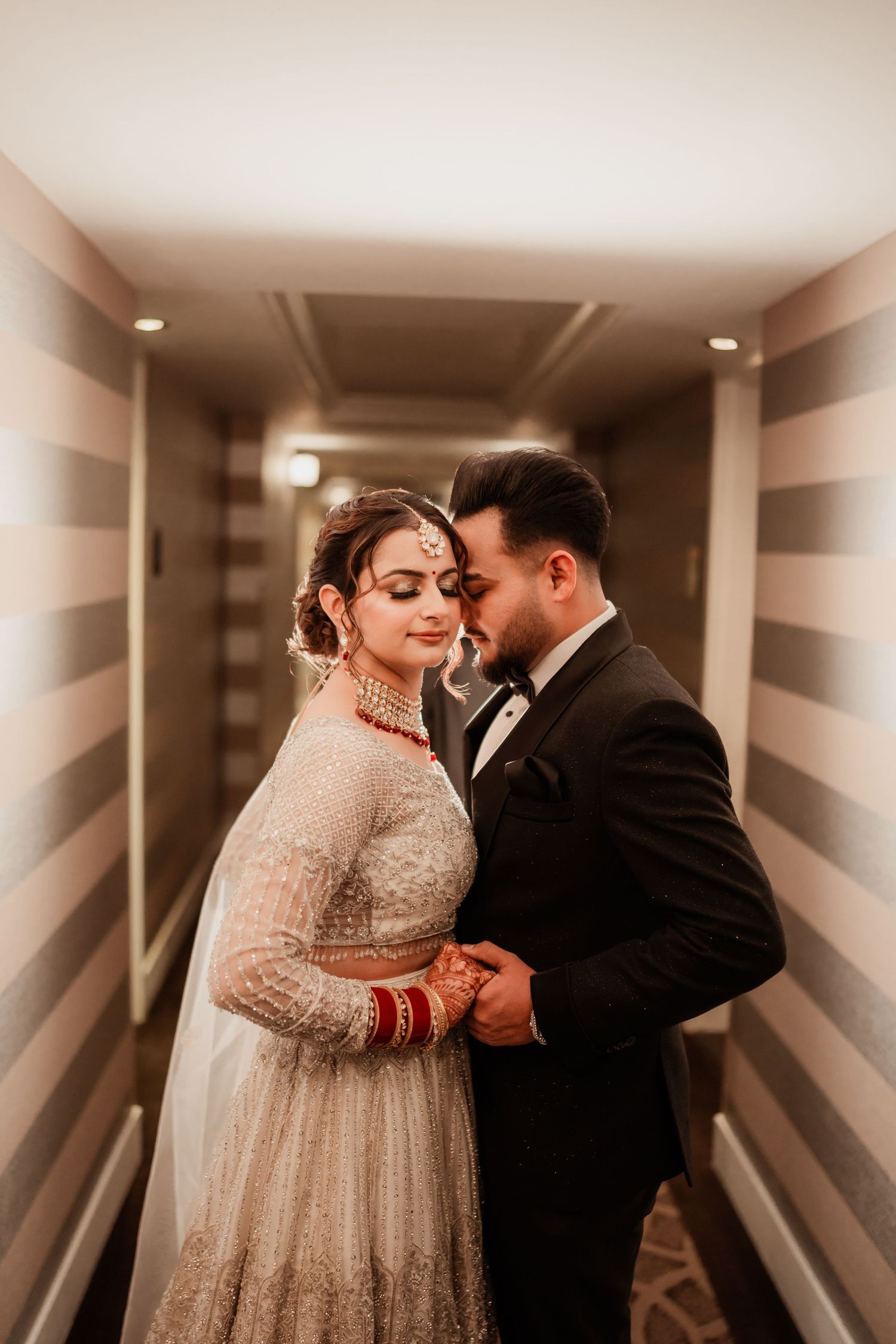A couple shares an intimate moment in a warmly lit hotel hallway.