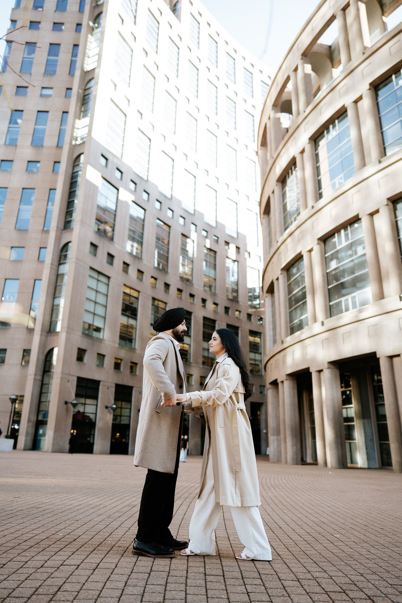 Two figures in white and black traditional dress stand in front of a modern architectural building with curved walls.
