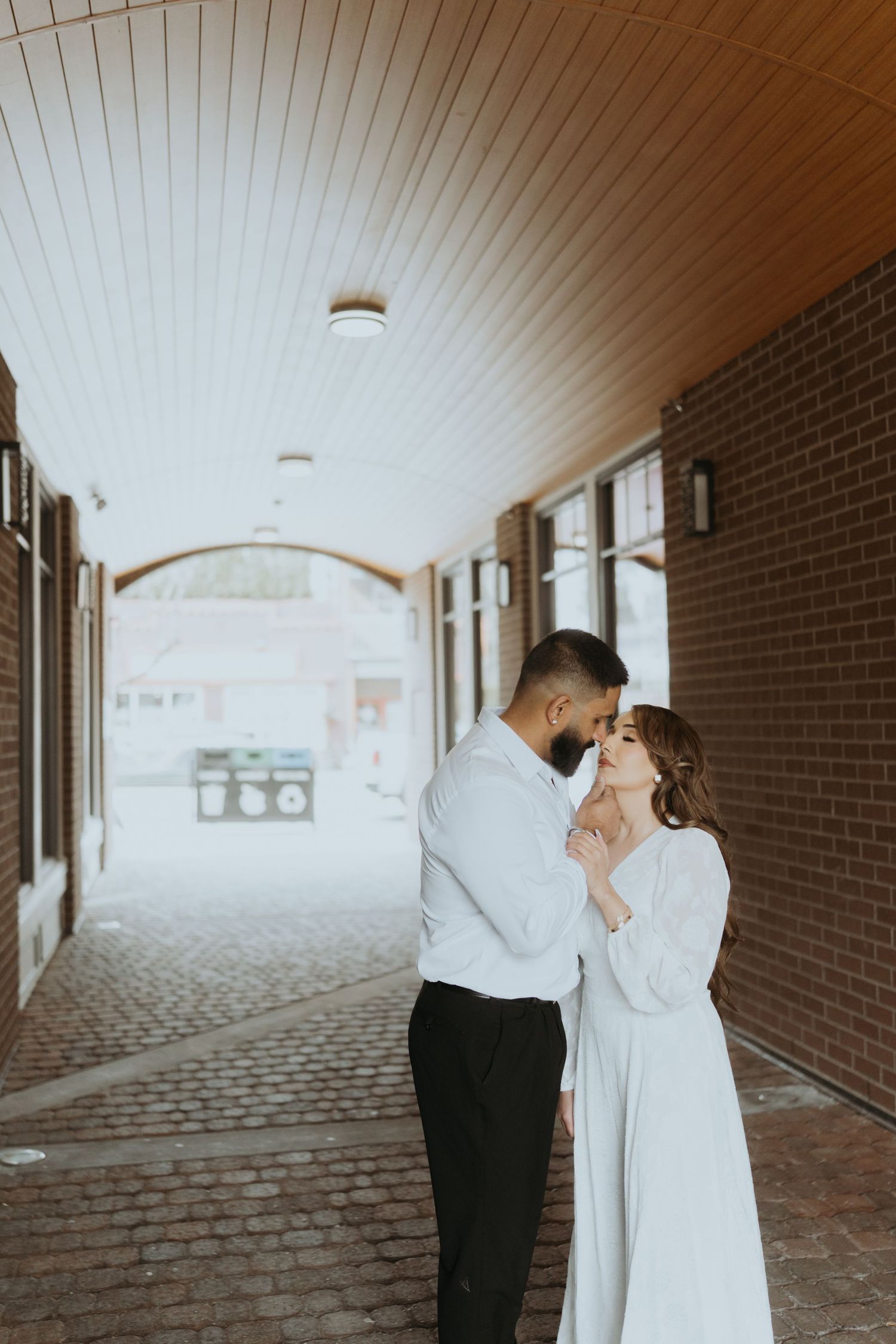 Couple shares tender moments in a brick-lined hallway with white paneled ceiling.