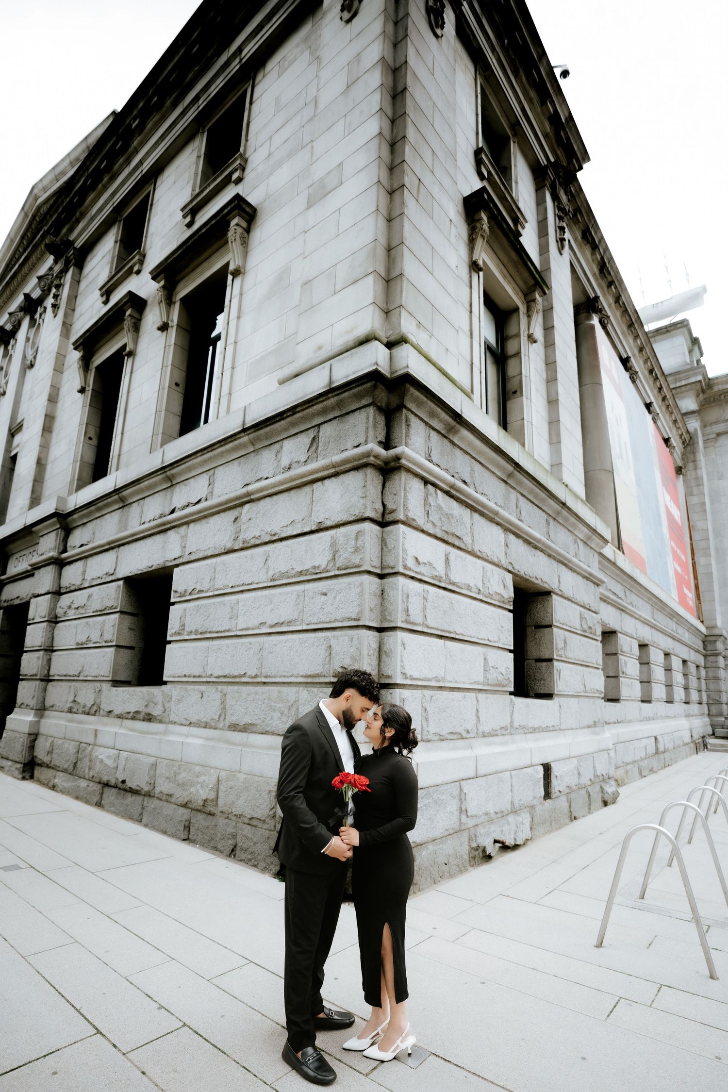 Romantic couple shares intimate moments against architectural backdrop in downtown setting.