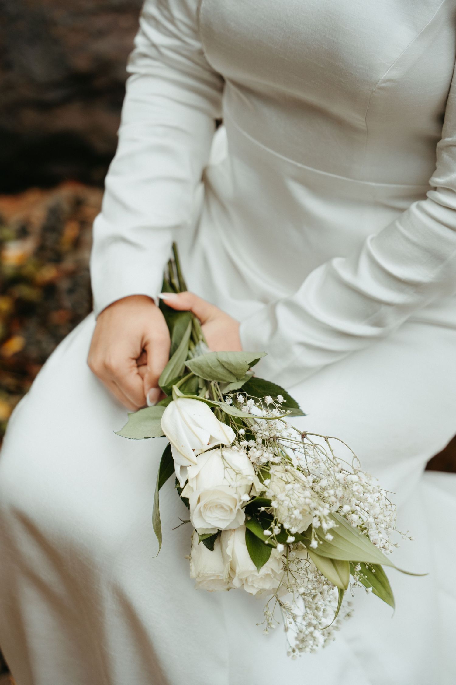 Close-up view of white roses and baby's breath flowers held against a white dress in natural lighting.