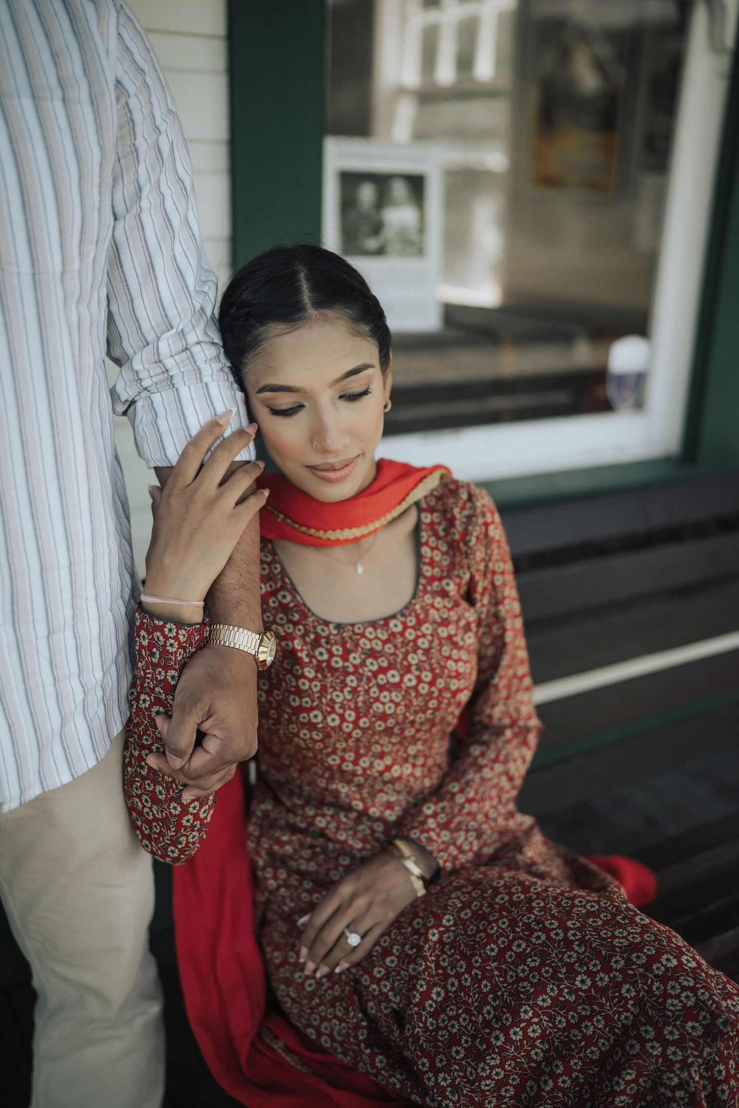 A person in a floral brown dress sits gracefully near a white pillar, looking down with a contemplative expression.