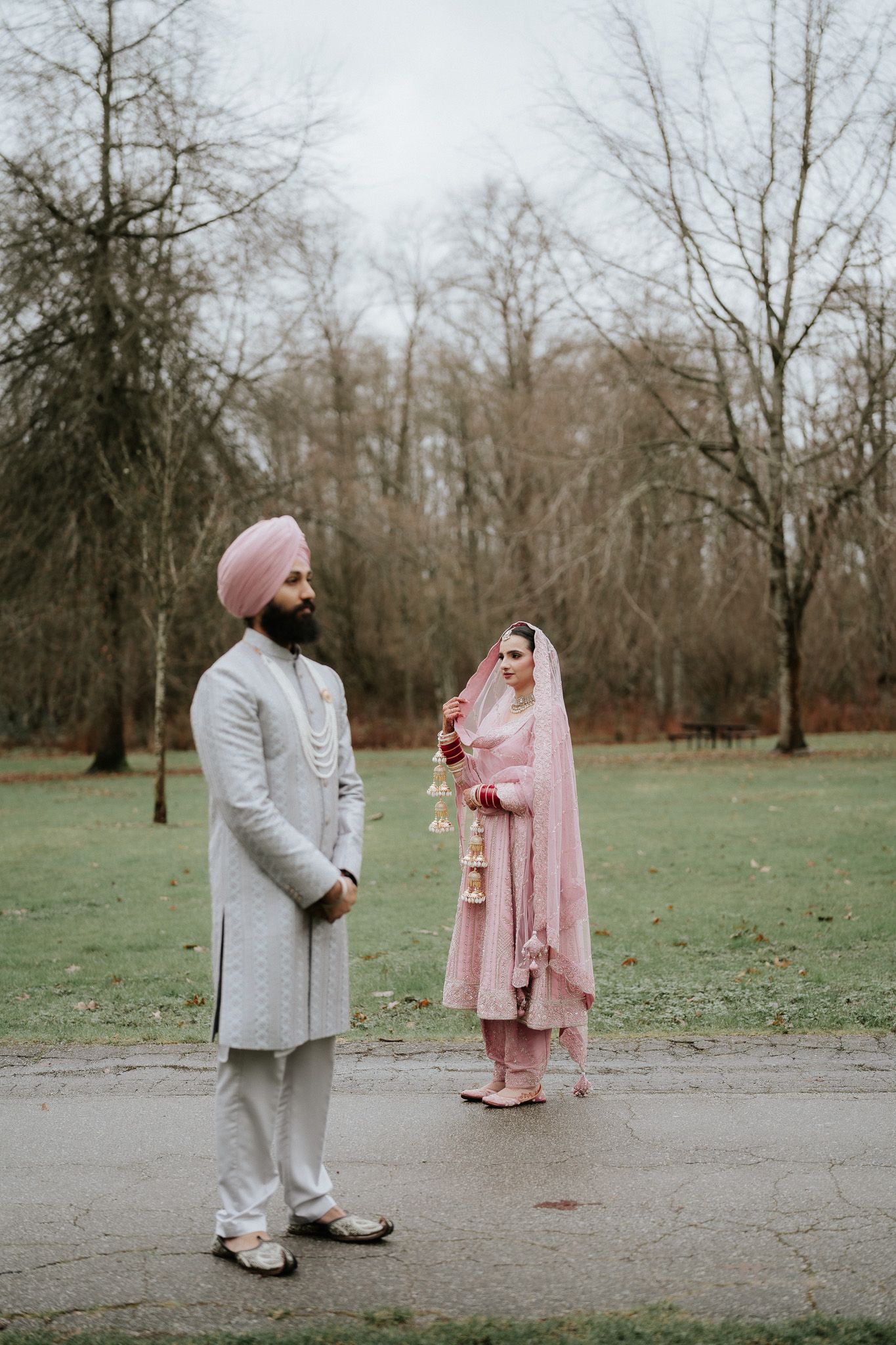 A couple in traditional South Asian wedding attire stand together in a park setting during winter.
