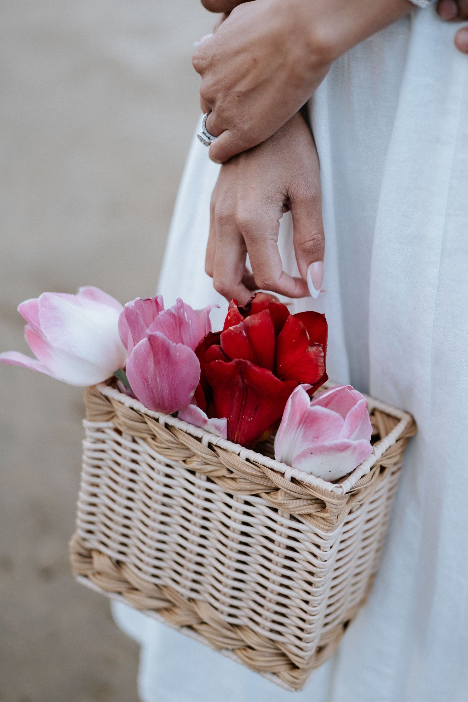 A woven wicker basket filled with pink and red rose petals held against a white dress.