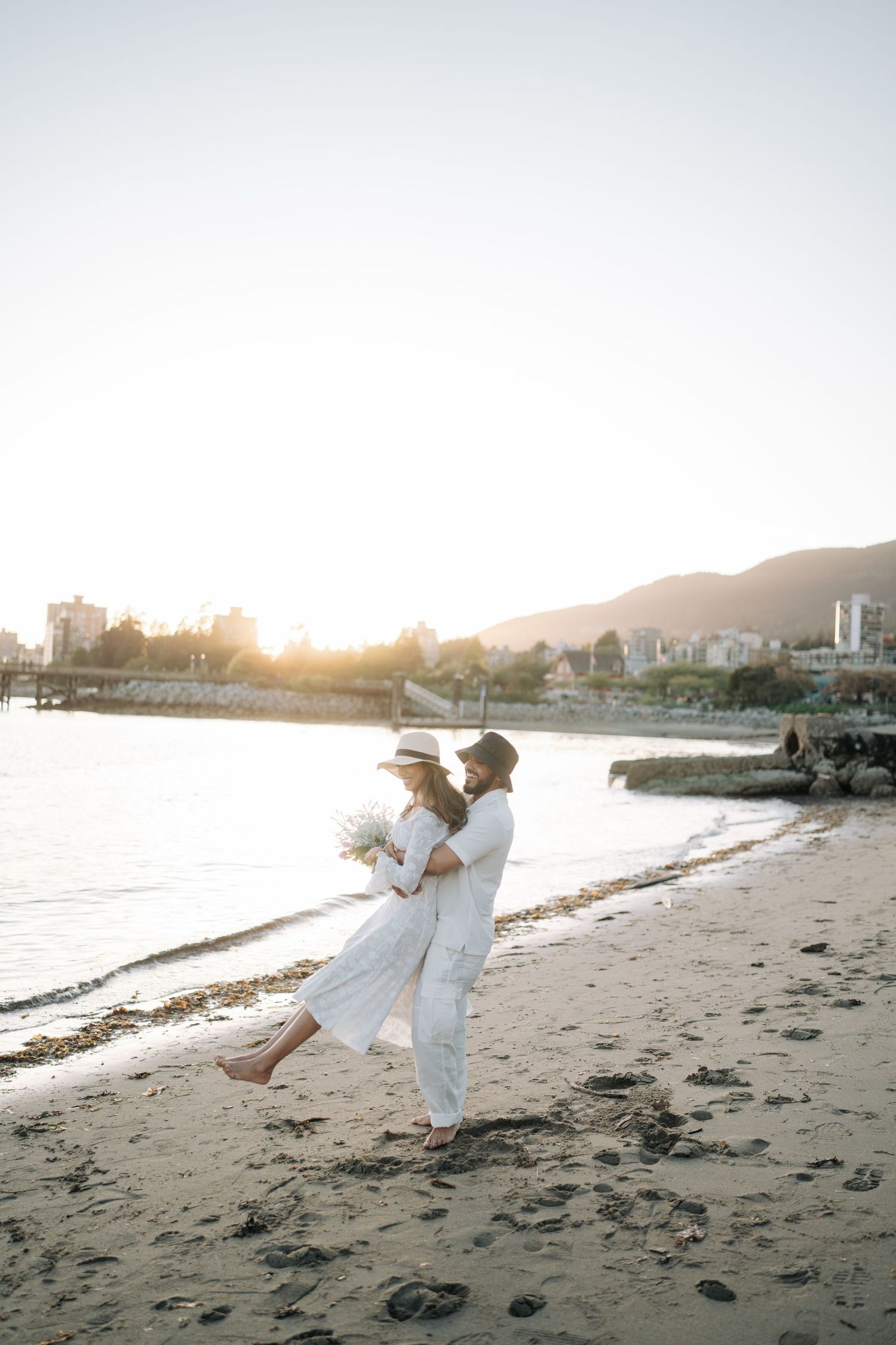 A couple in white clothing dances gracefully along a scenic beach at sunset, creating romantic silhouettes against the shore.