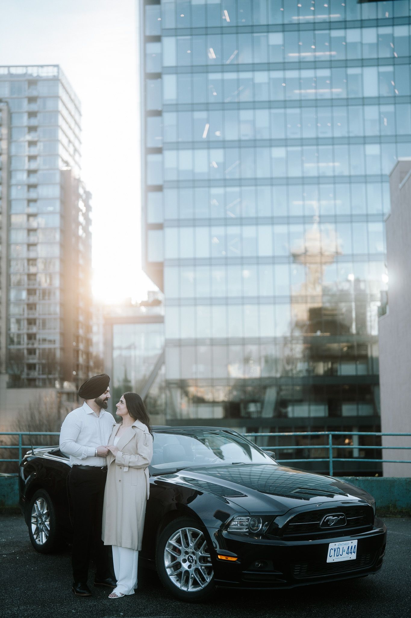 A black Ford Mustang parked in front of a modern glass building at sunset with figures in white clothing.