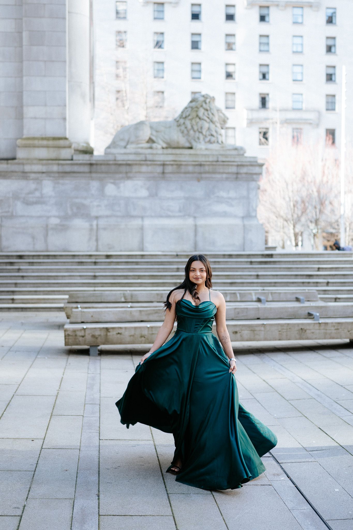 A flowing emerald evening gown creates an elegant swirling motion against a classical architectural backdrop.