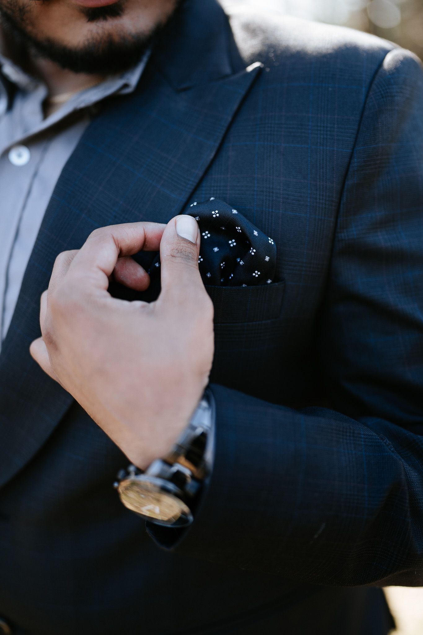 Close-up of a navy suit jacket with a patterned pocket square and gold watch visible.