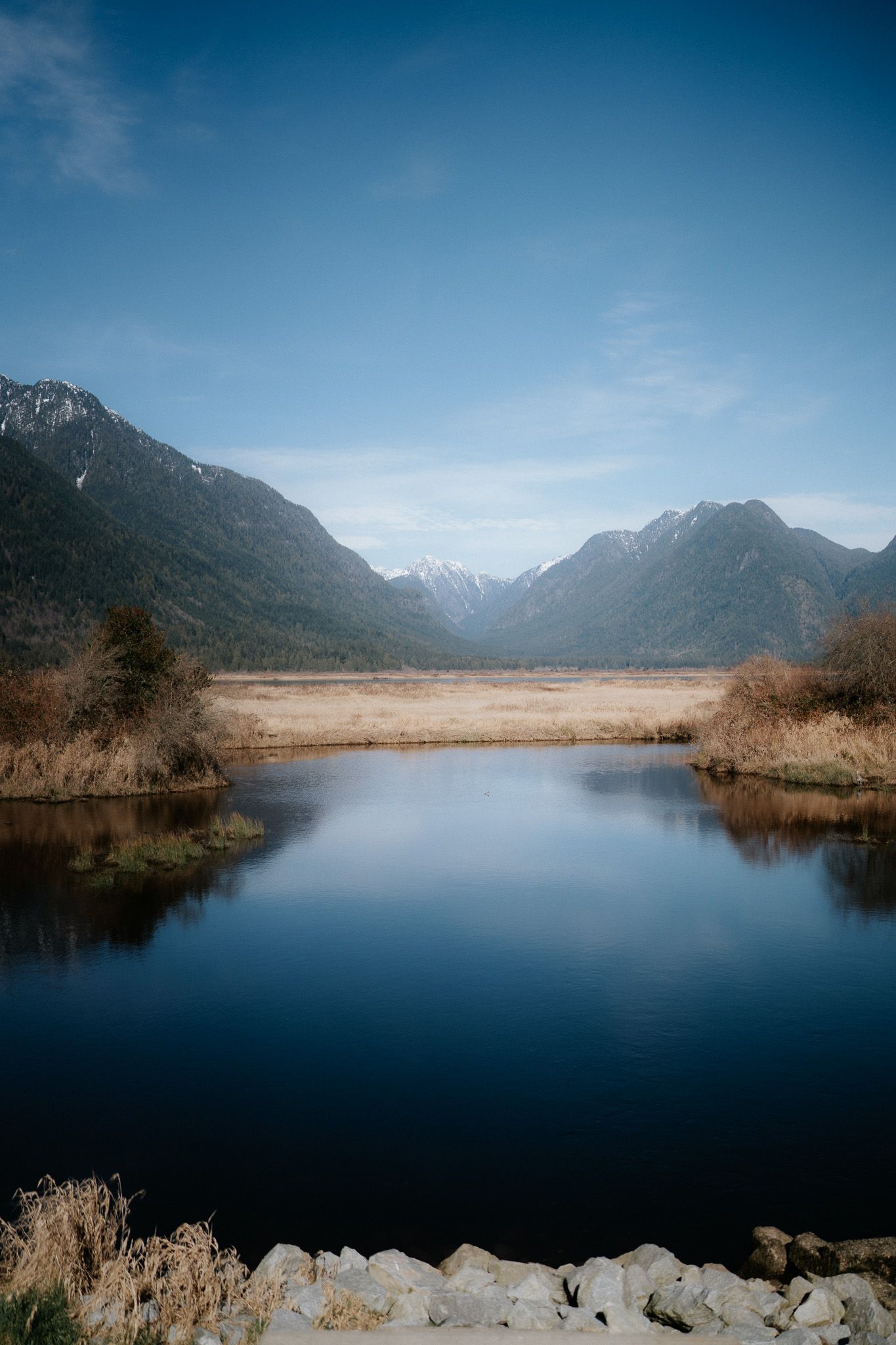 A serene mountain lake with calm reflective waters surrounded by rugged peaks and autumn foliage in the wilderness.
