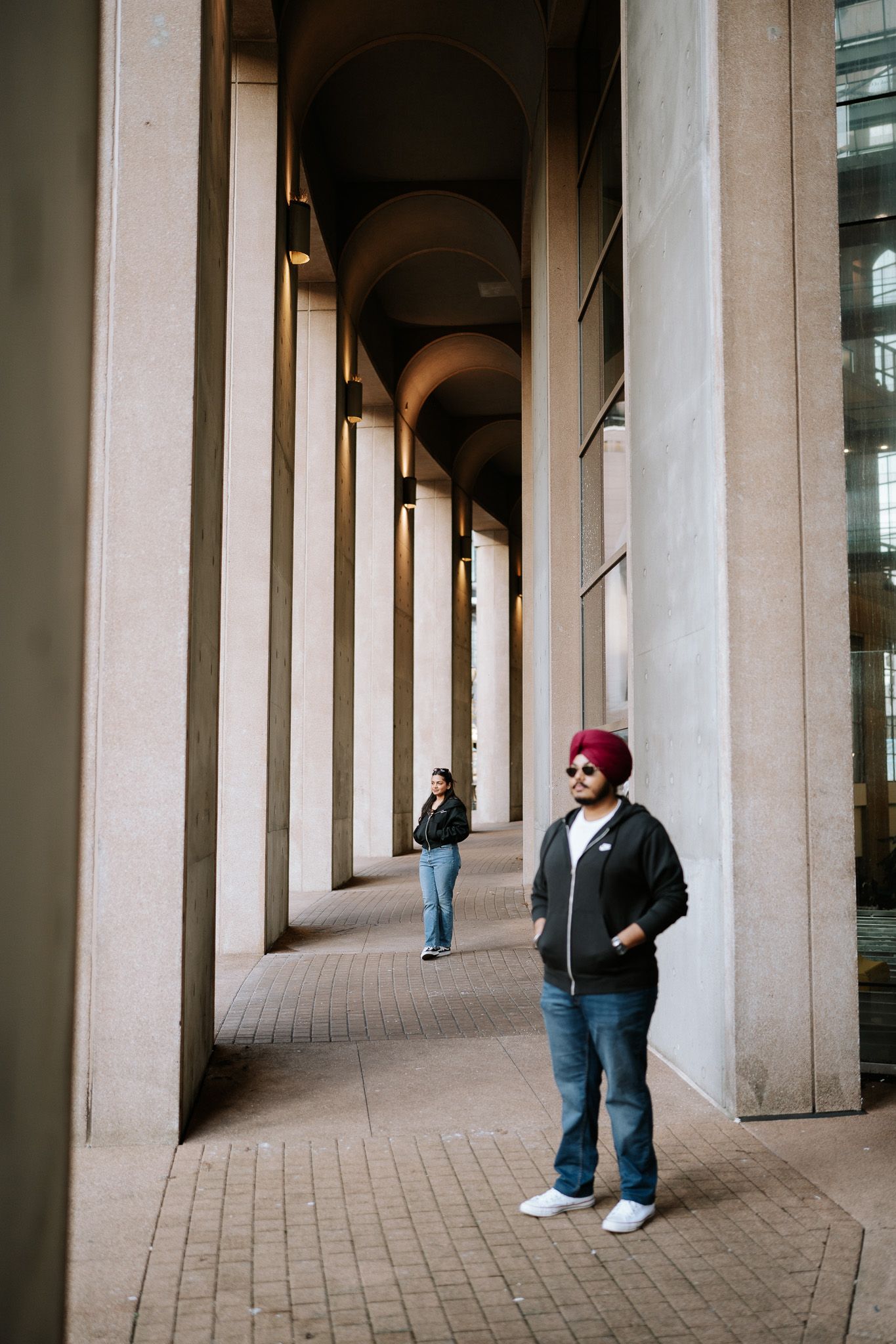 A person stands in a modern architectural colonnade with repeating arched columns and stone flooring.