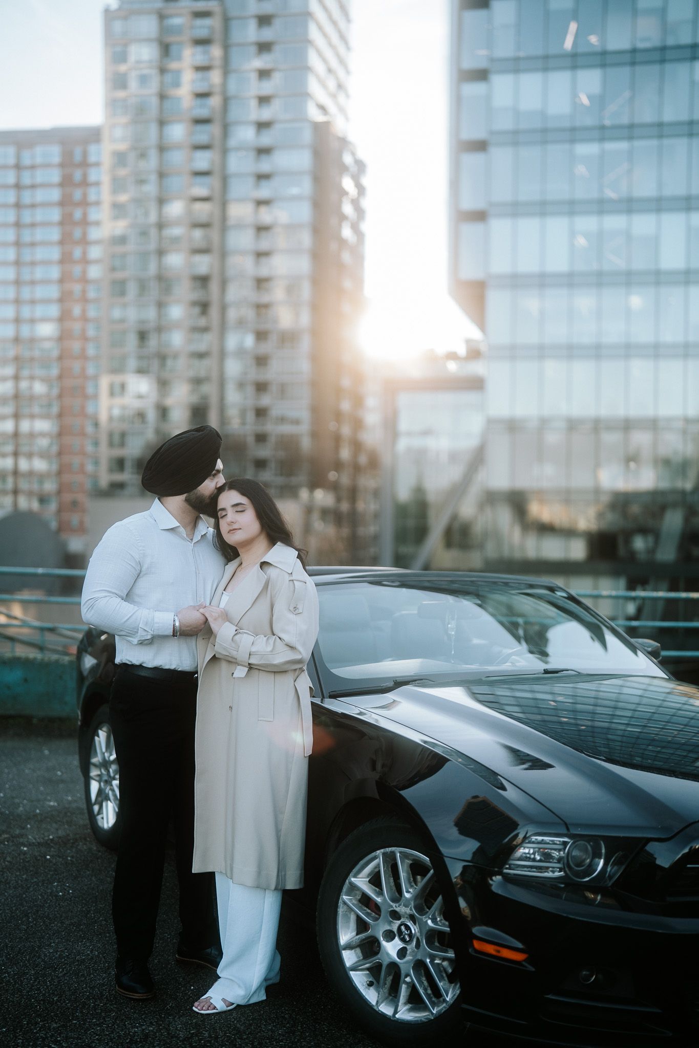 A sleek black sports car parked near a glass building with people in formal attire standing beside it.