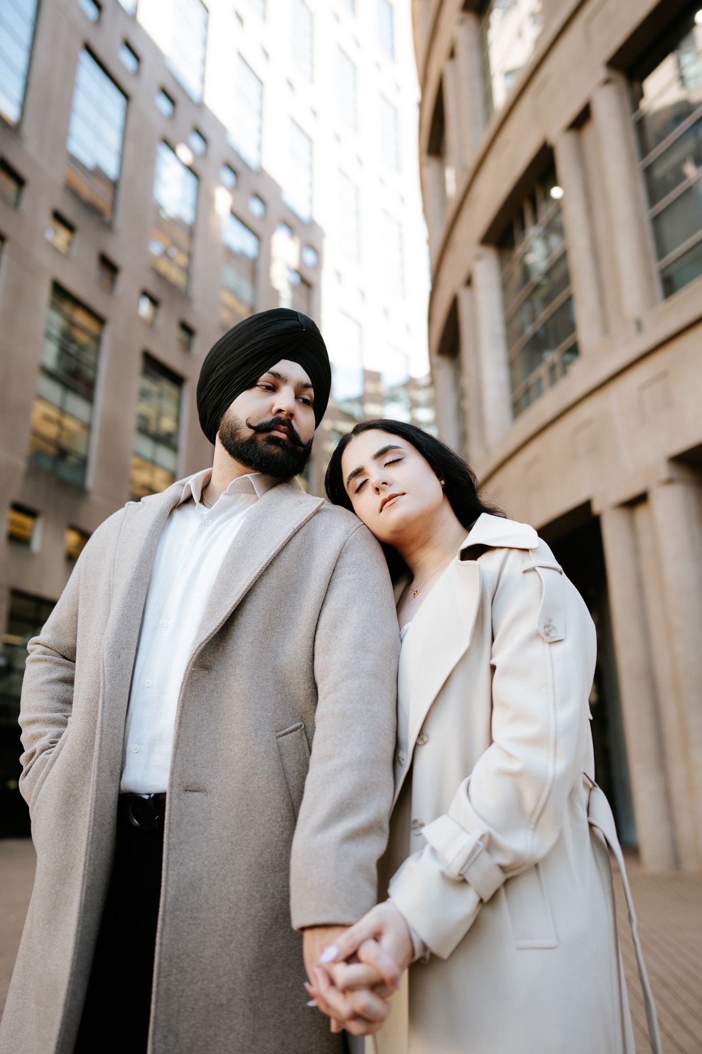 Couple in coordinated beige and white outfits pose against architectural columns in an urban setting.
