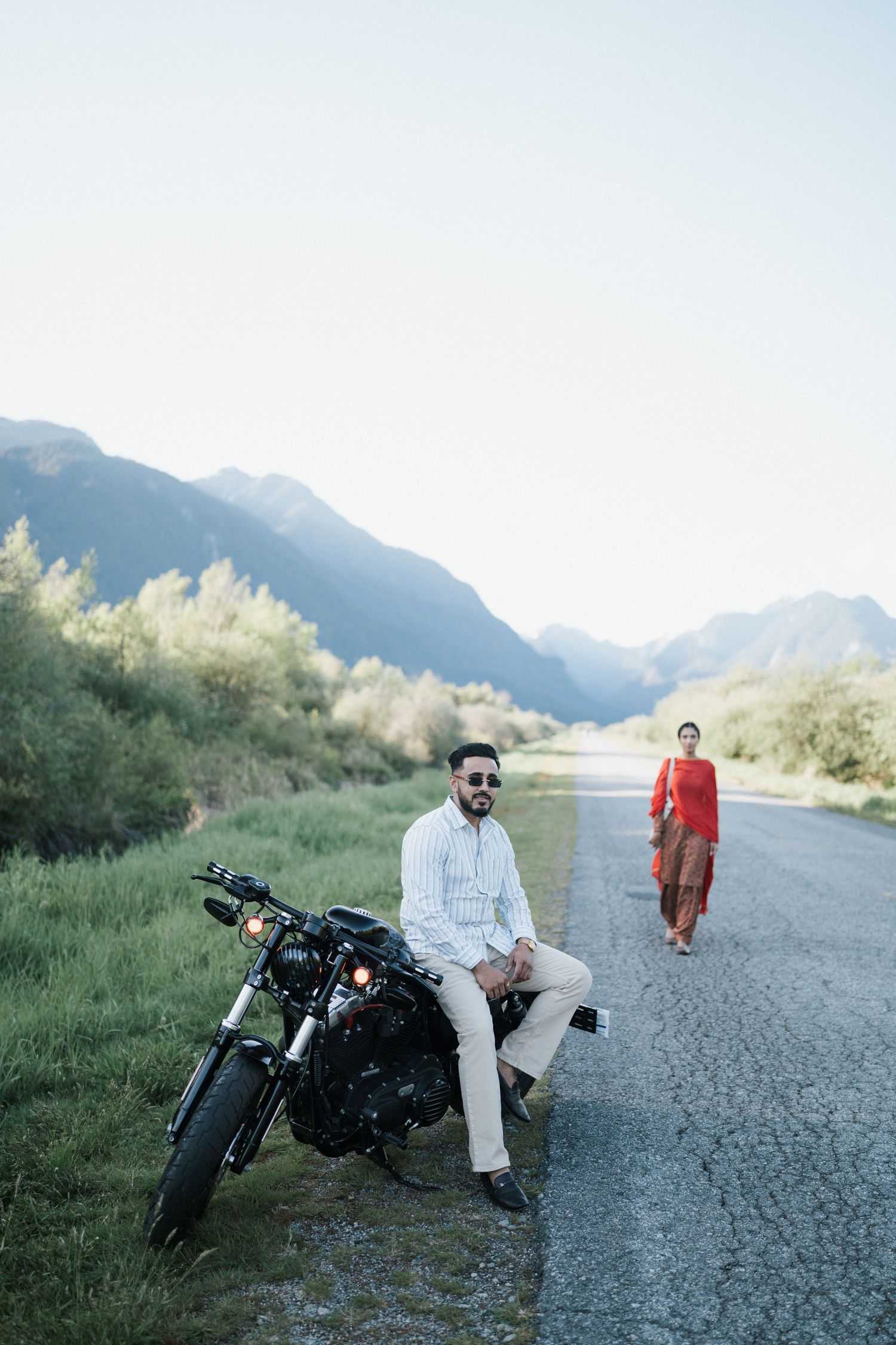 Motorcyclist takes a break on a gravel road surrounded by scenic mountain landscape and lush greenery.