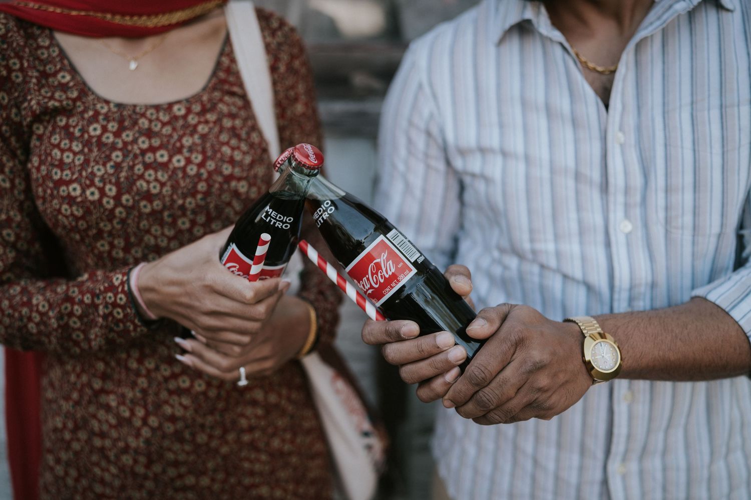 Two people hold glass Coca-Cola bottles while standing together in casual attire.
