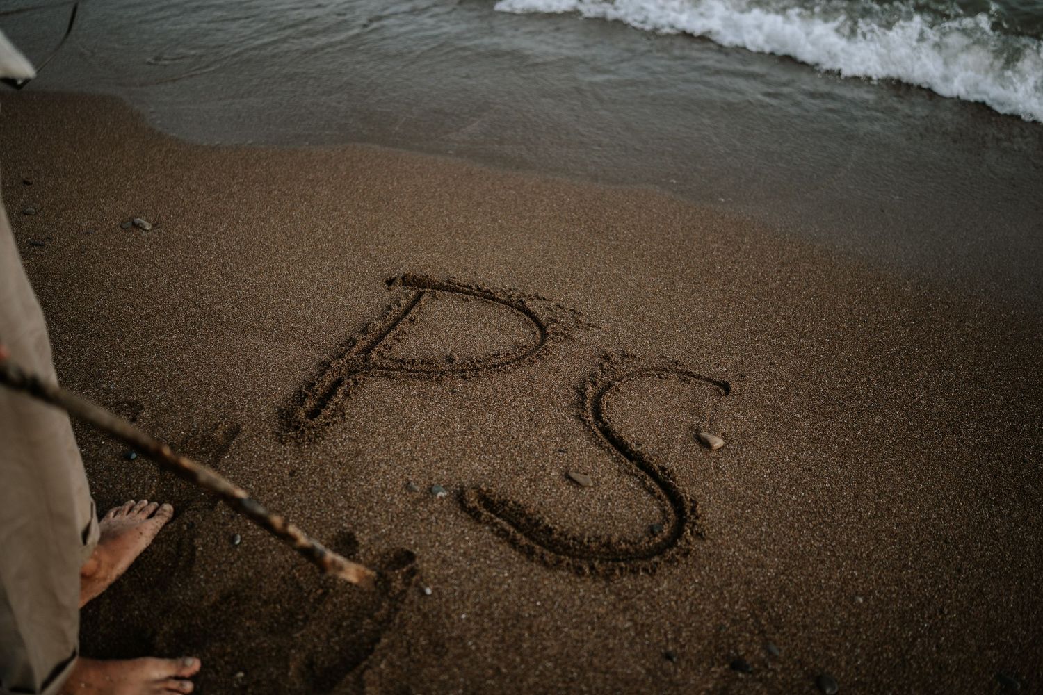 Heart shape drawn in wet sand on beach with ocean waves in background.