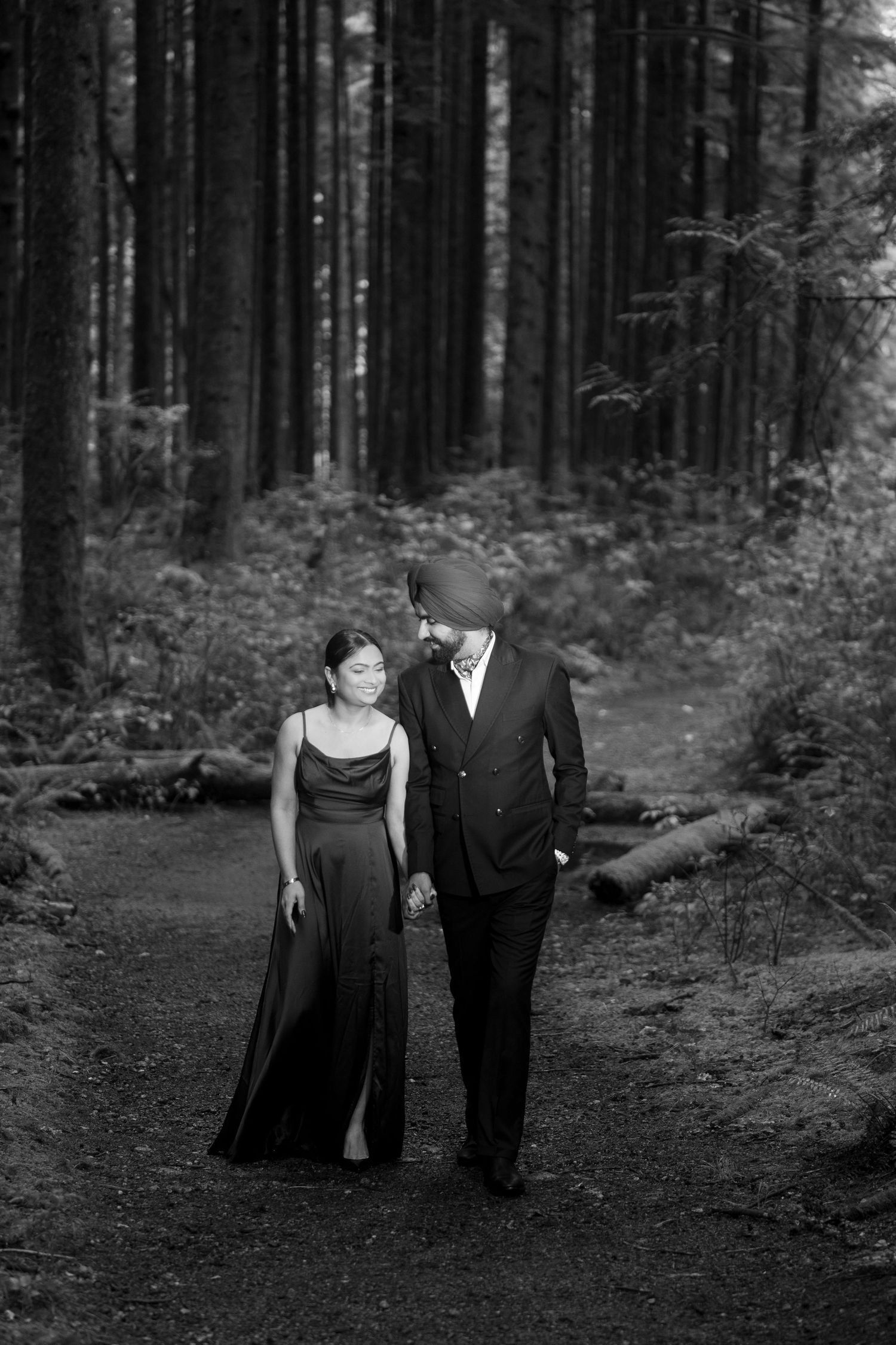 Black and white portrait of couple walking together on a forest trail.