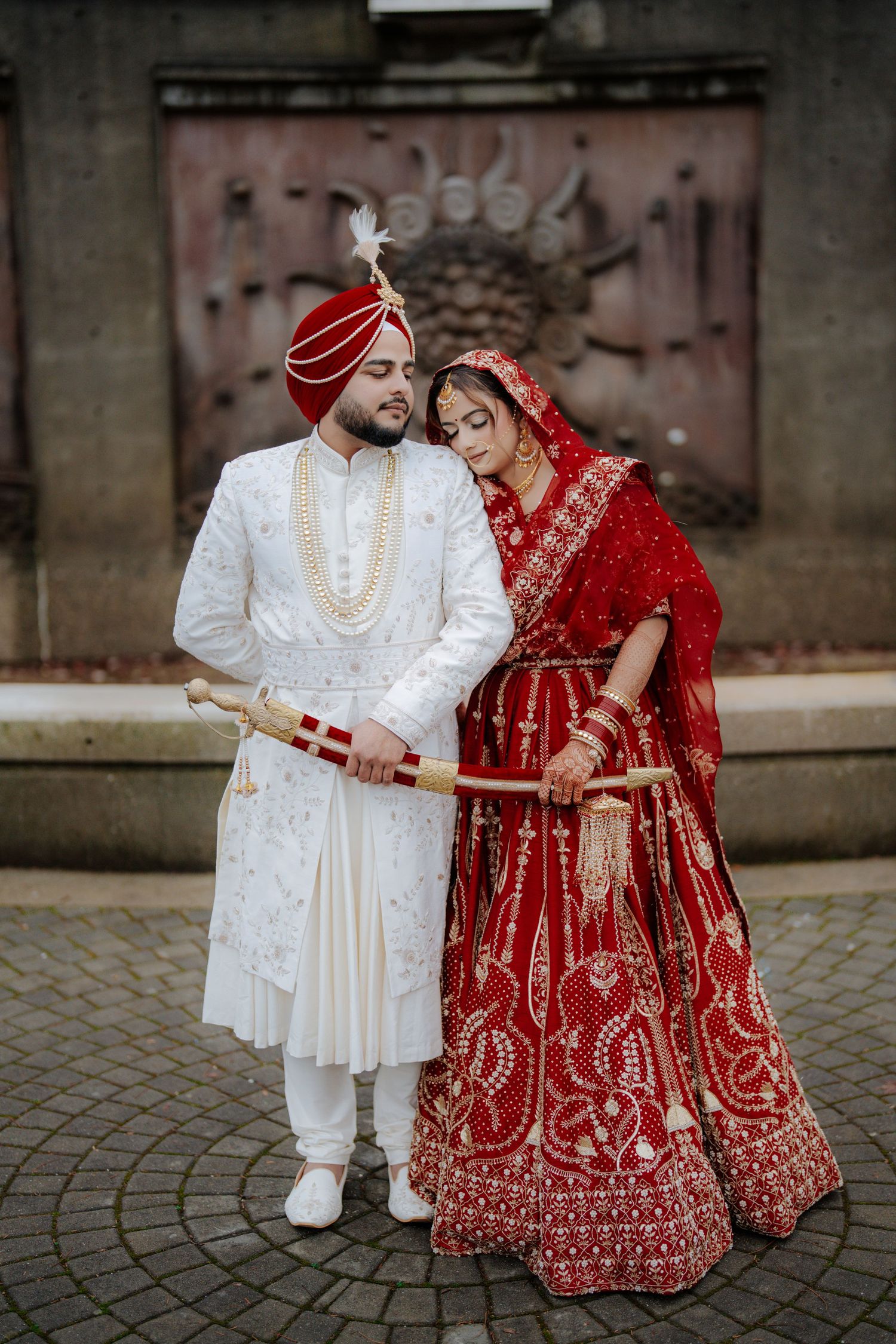 Wedding couple in traditional Indian attire sitting on cobblestone pavement during ceremony.