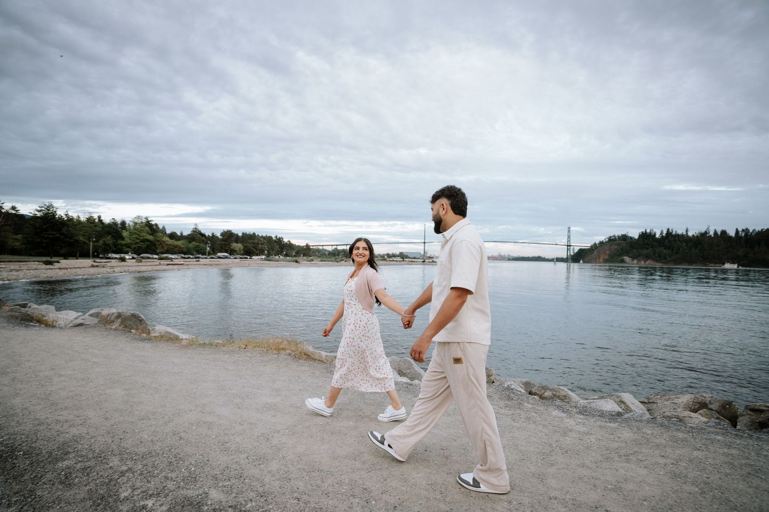 A romantic beach photoshoot featuring two people in coordinated white outfits near the water.