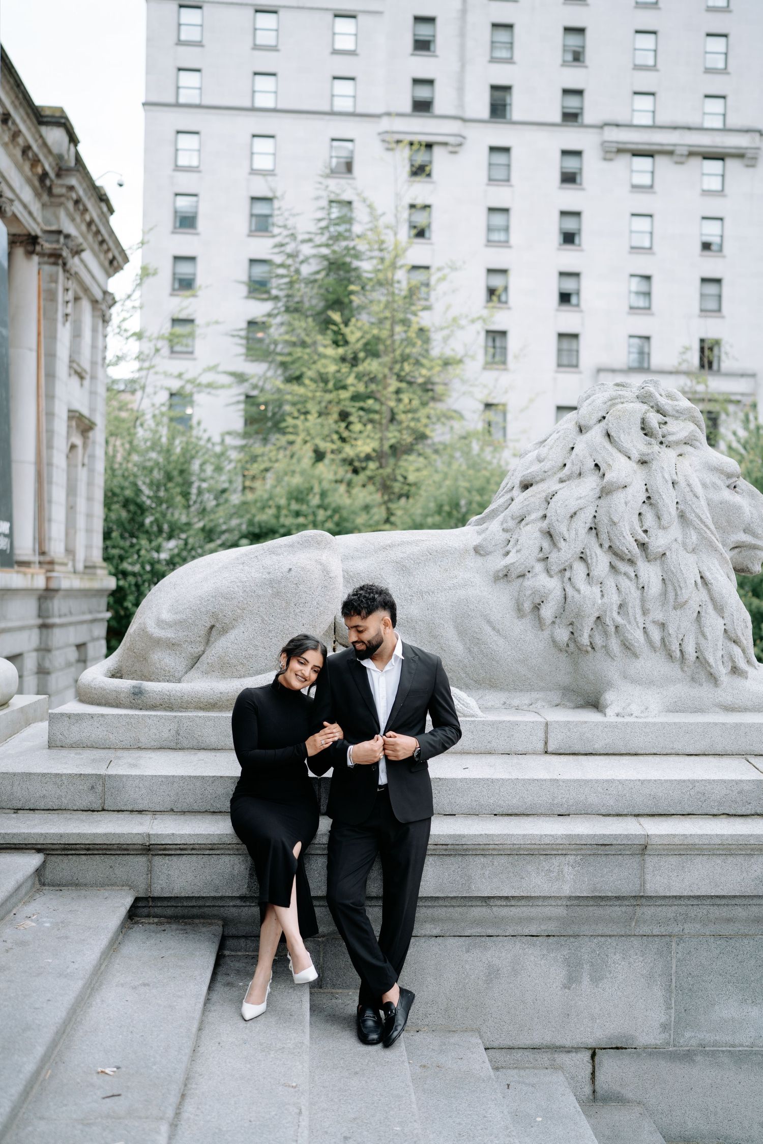 Two people share tender moments on marble steps near decorative stone sculptures.