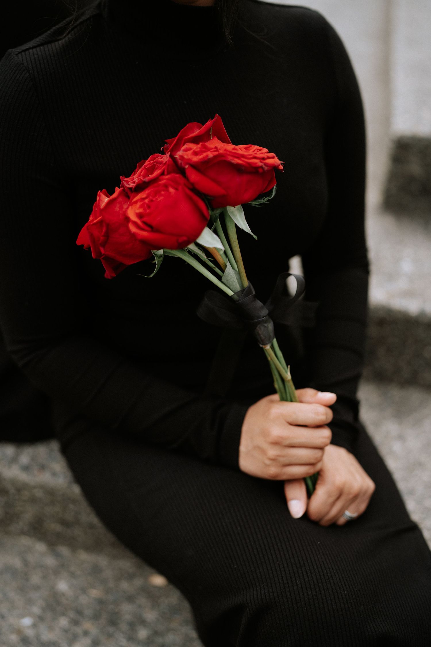 A person in black holds a bouquet of vibrant red roses against a light background.