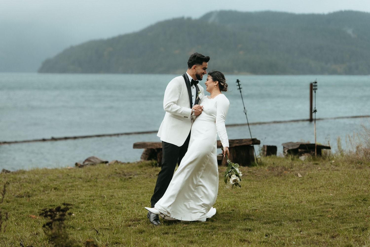 Romantic coastal wedding photos captured on a misty green hillside overlooking the ocean.