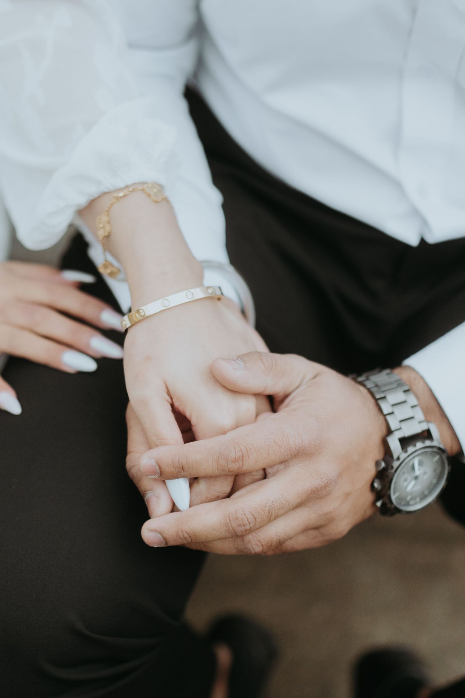 Close-up of hands holding each other tenderly, showing jewelry and a watch.