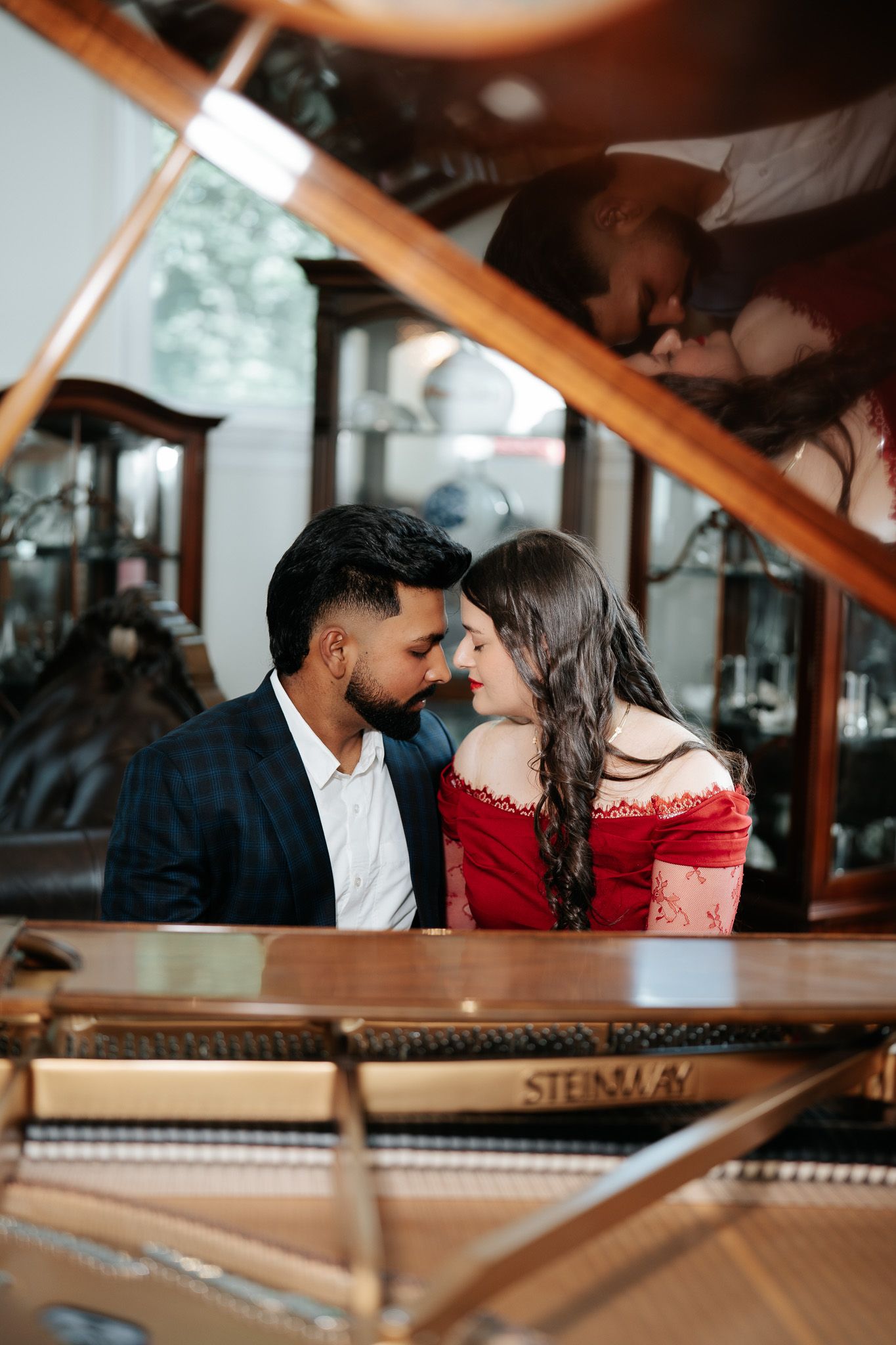 Romantic couple sharing an intimate moment framed by the open lid of a Steinway grand piano.