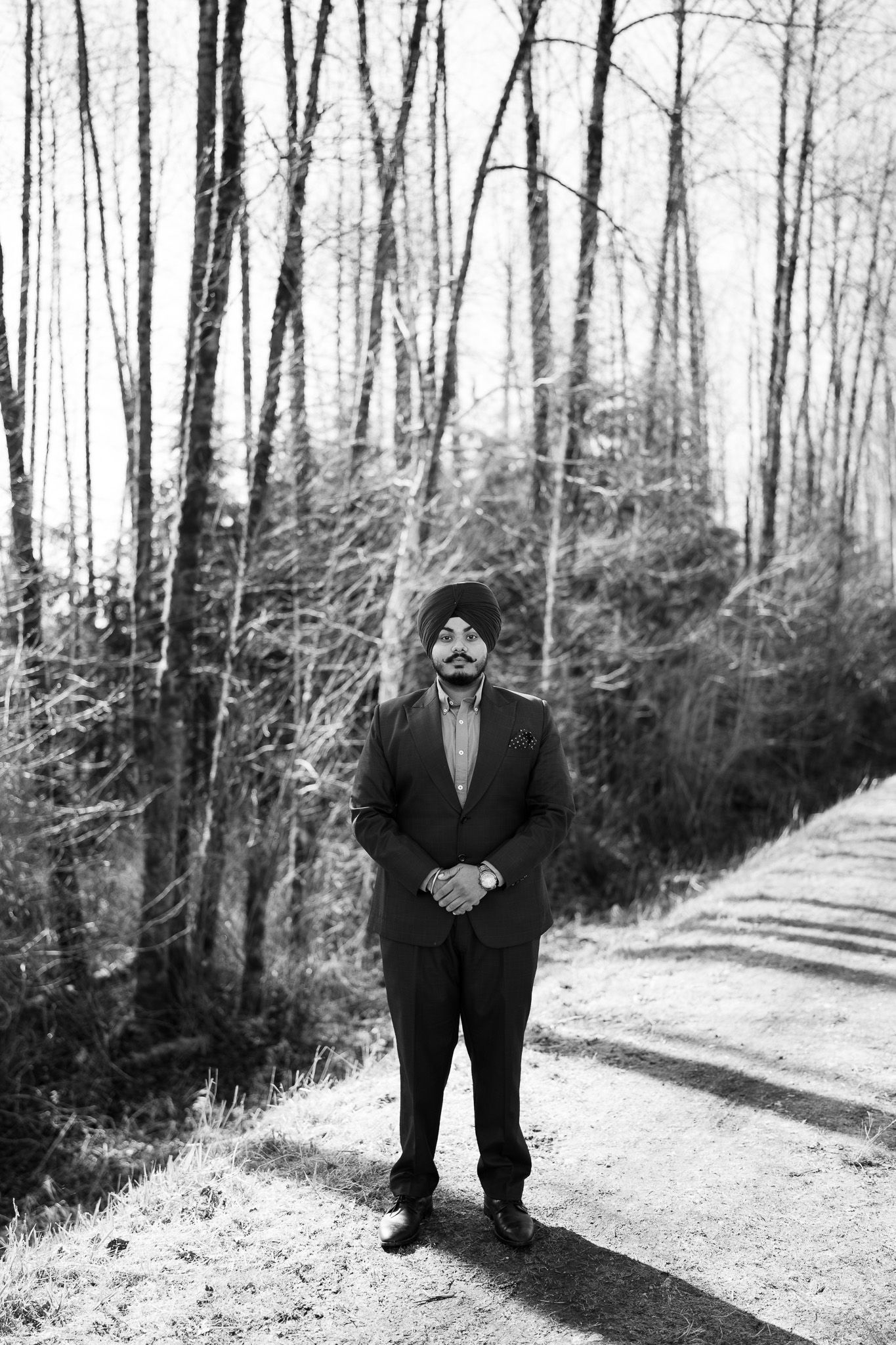 A black and white photo shows a figure in a dark suit standing on a wooded path surrounded by bare winter trees.