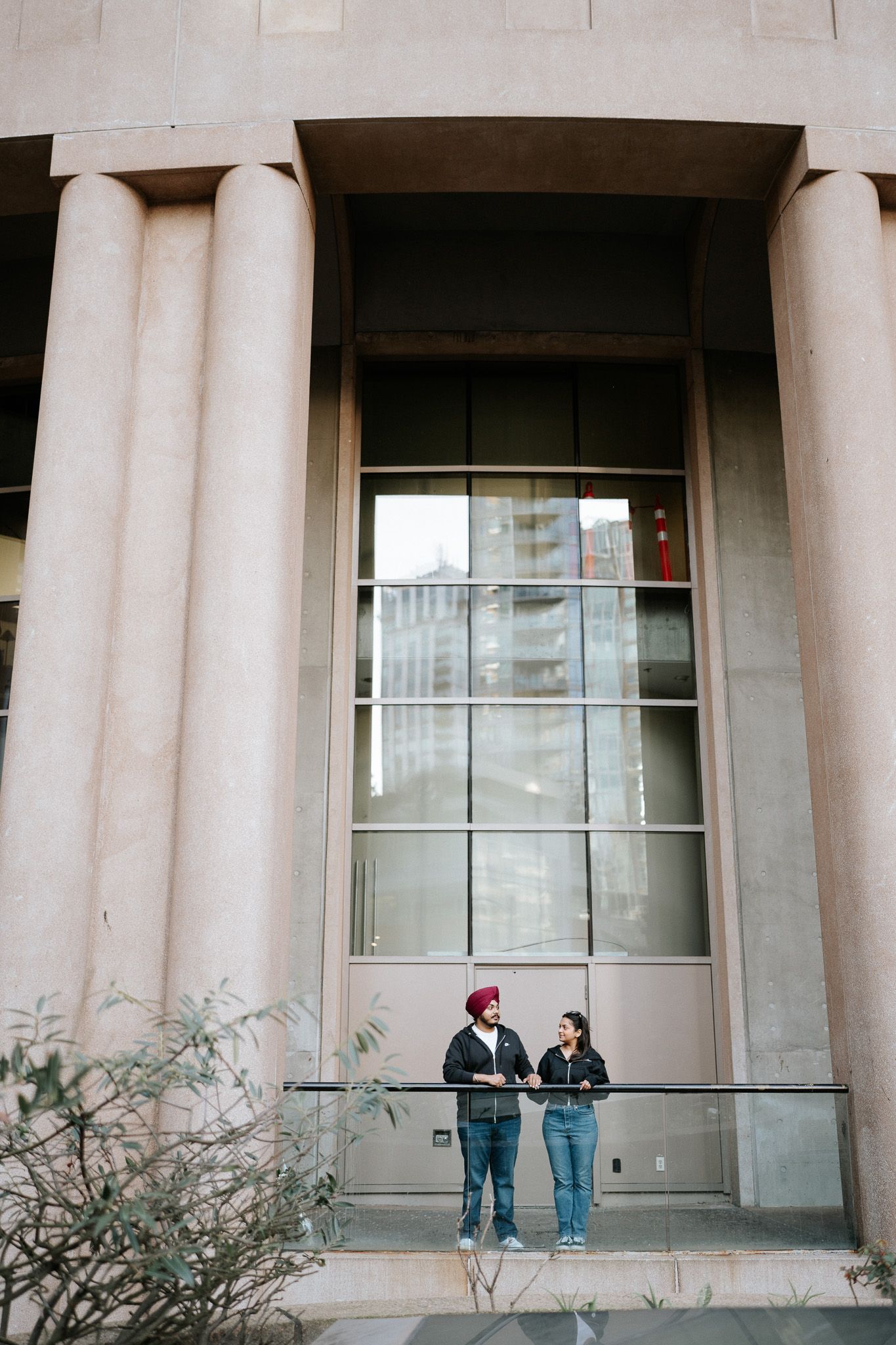 People stand in conversation beneath tall stone columns of a building's classical facade.