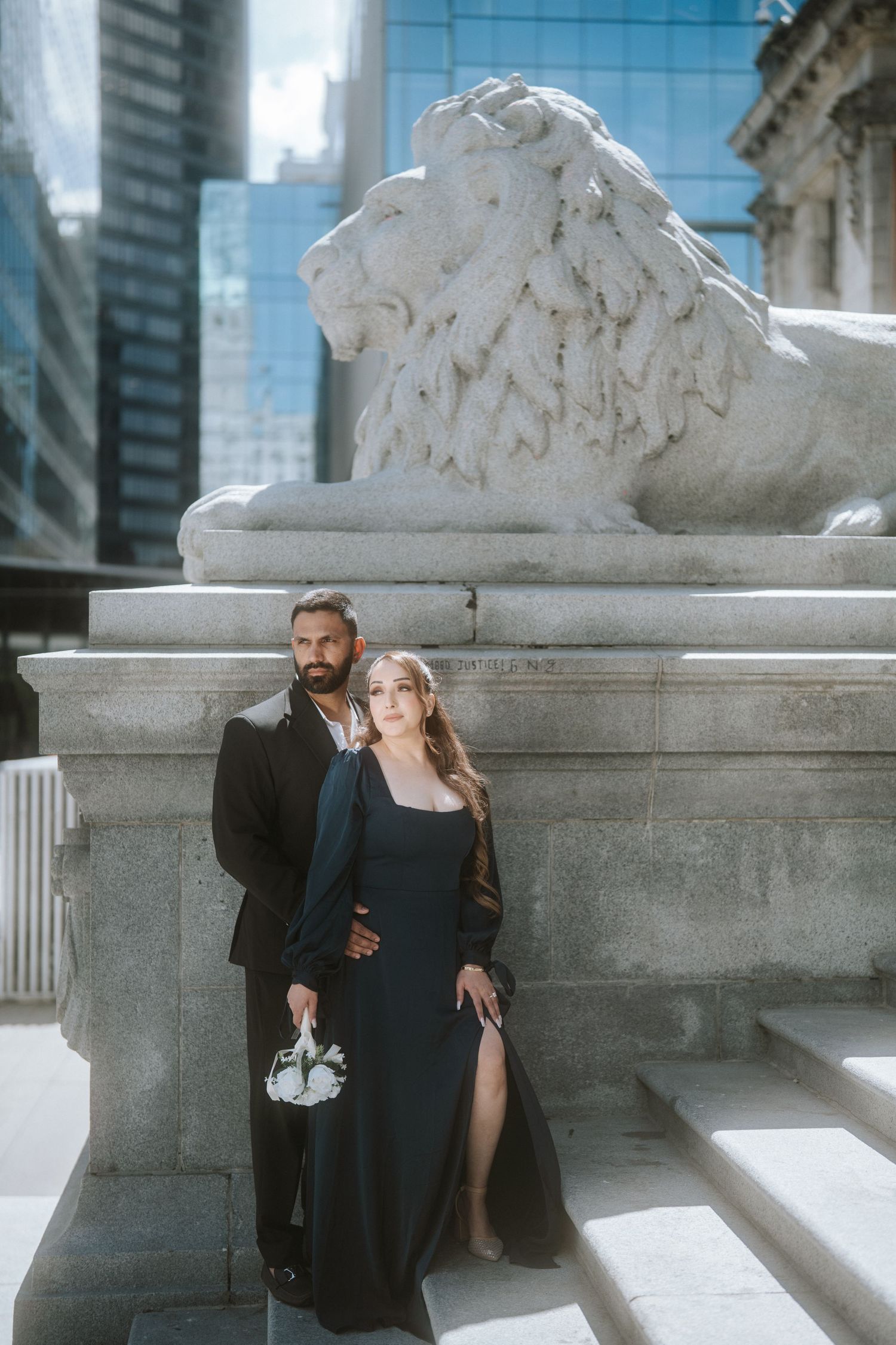 Elegant couple in black attire posing before a stone lion sculpture at the New York Public Library.