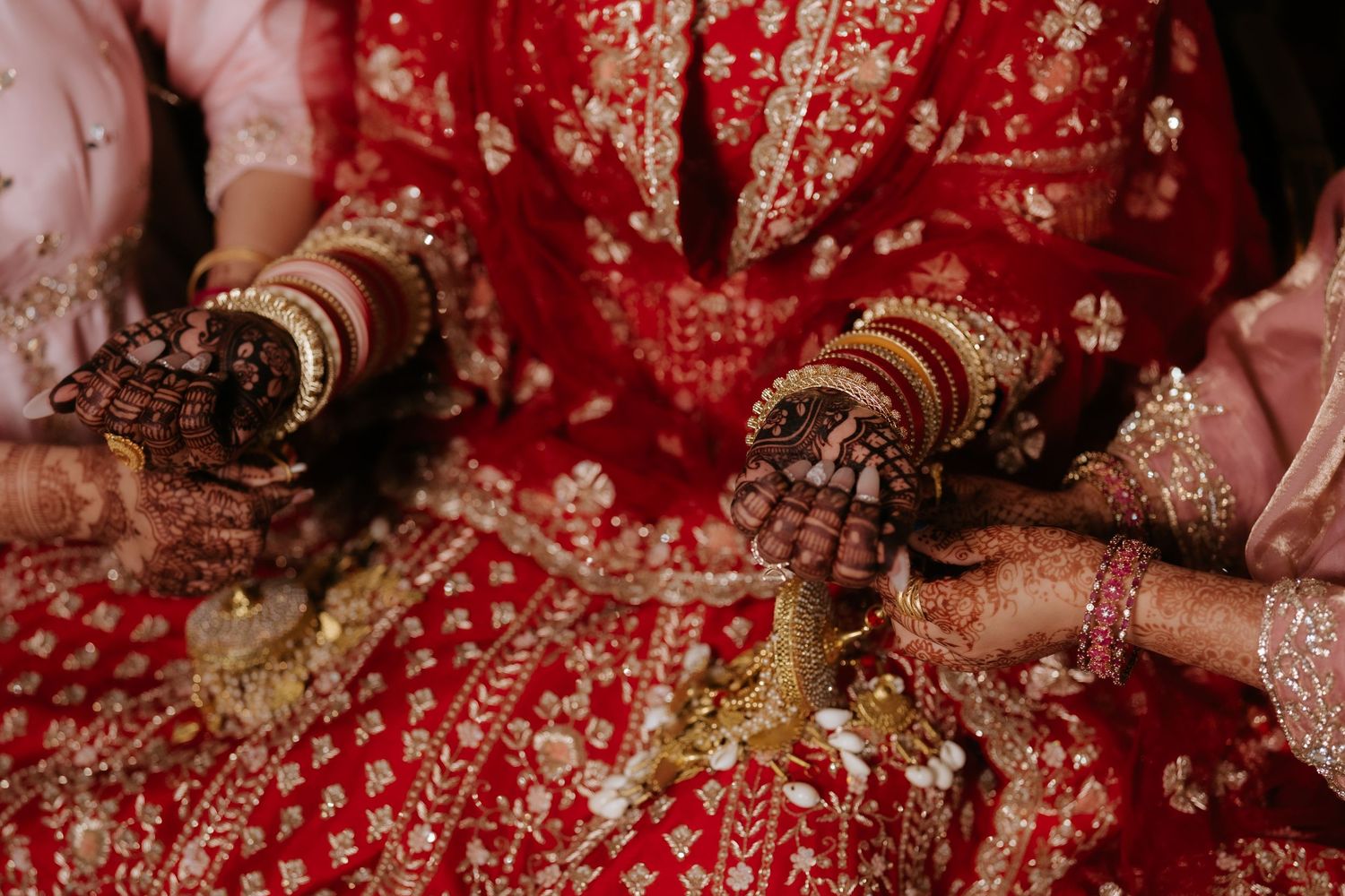 Indian bride in red lehenga with gold embroidery, hands adorned with mehndi and bangles during wedding ceremony.