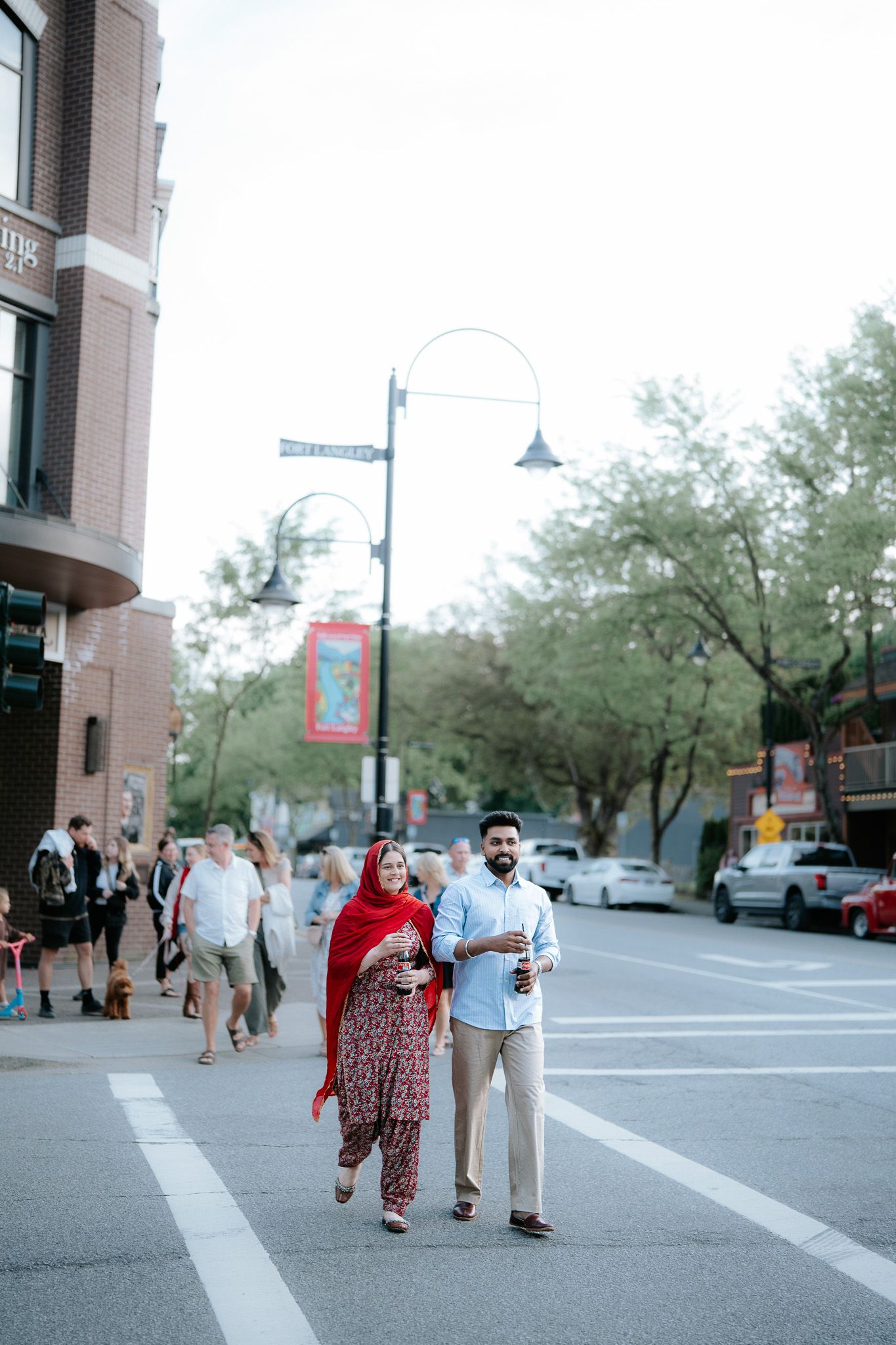 South Asian couple walking together on urban street, woman in red dupatta and floral salwar, man in blue shirt.