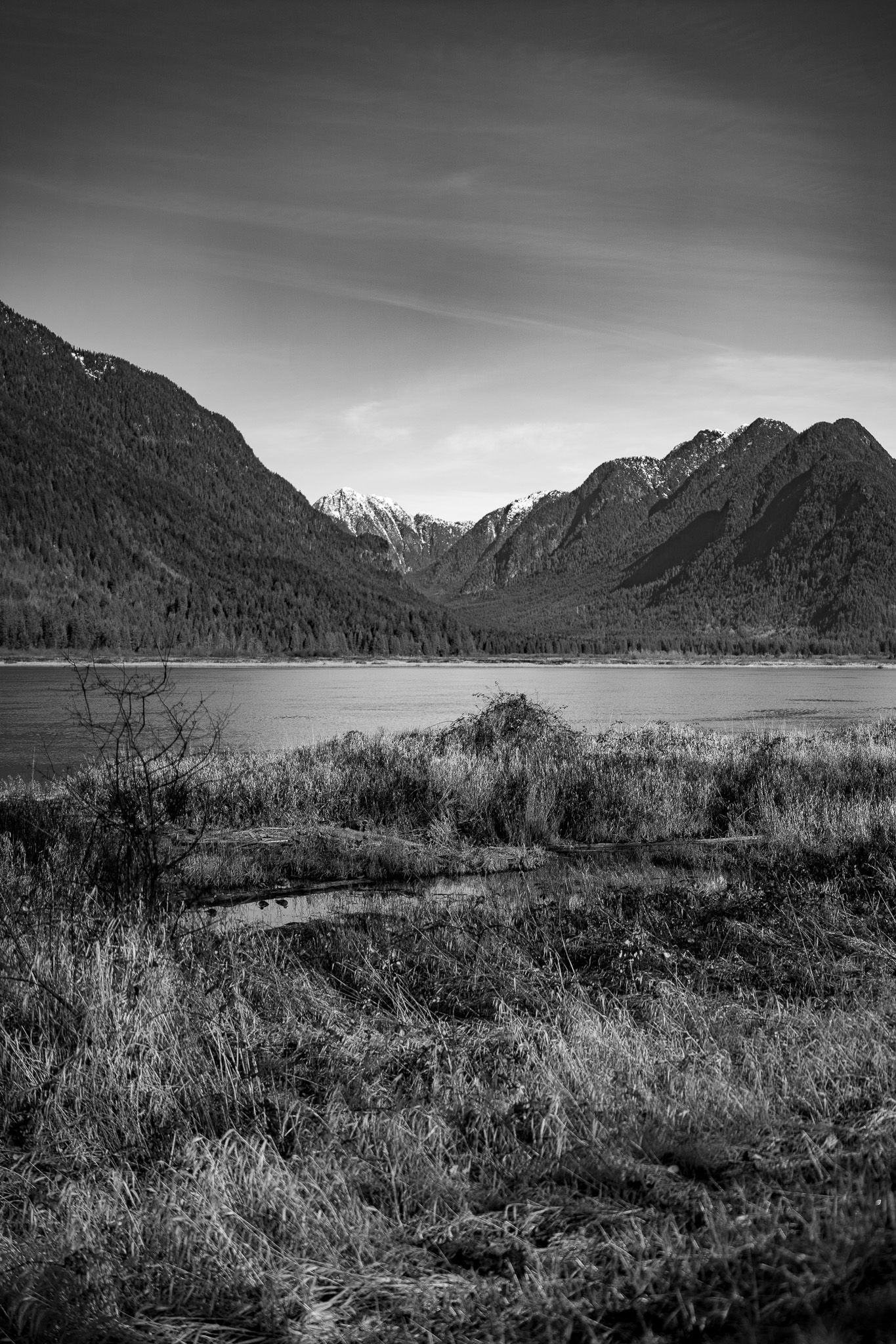 A black and white panoramic view of a remote mountain lake surrounded by rugged peaks and wild grasslands.