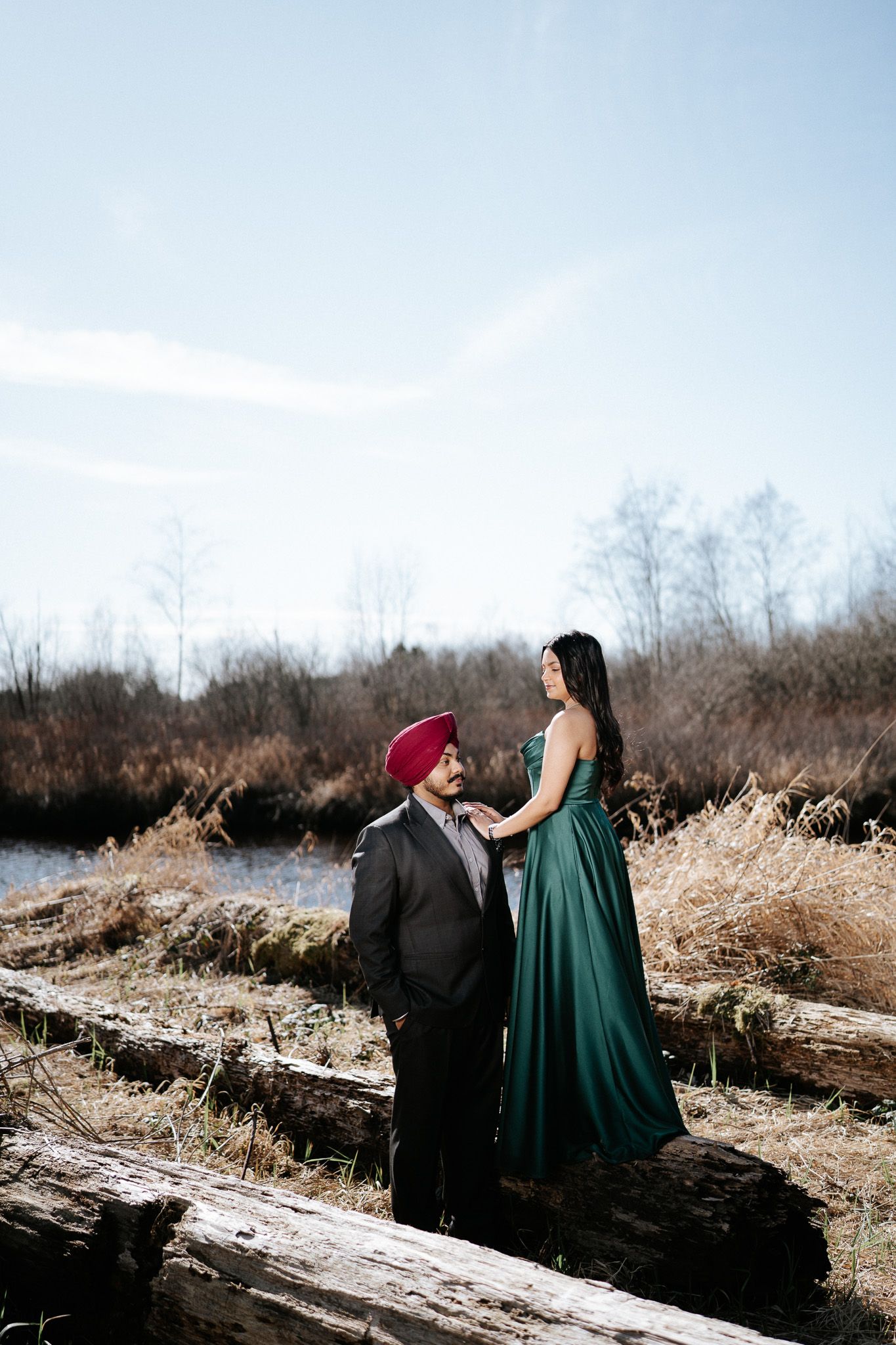 Two people in formal attire walk along a snowy path surrounded by winter foliage in a romantic outdoor setting.