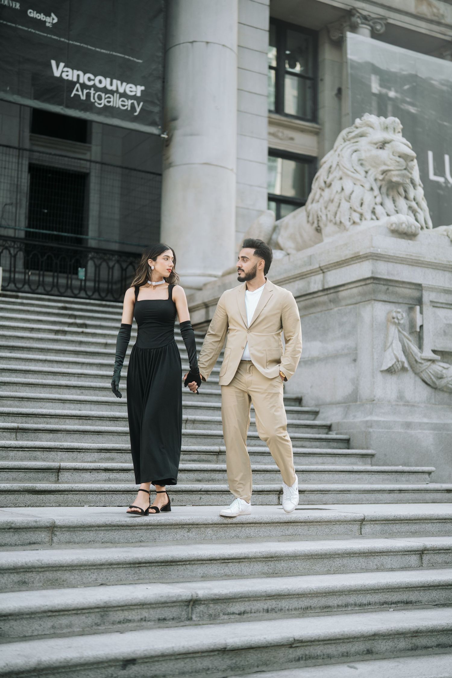 Couple standing on the steps of Vancouver Art Gallery in contrasting black dress and beige suit.