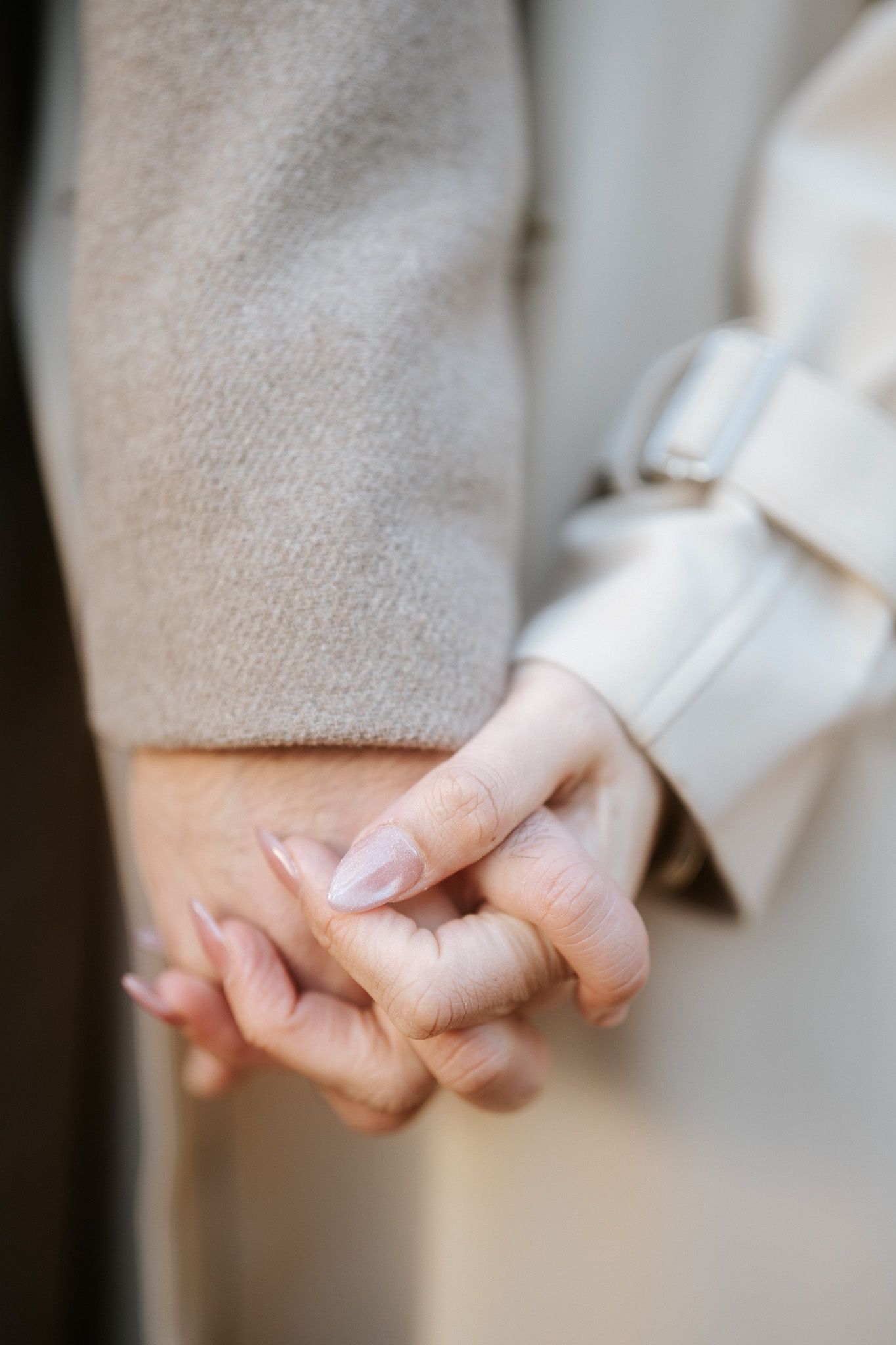 A close-up view of two hands tenderly clasped together against a soft beige background.