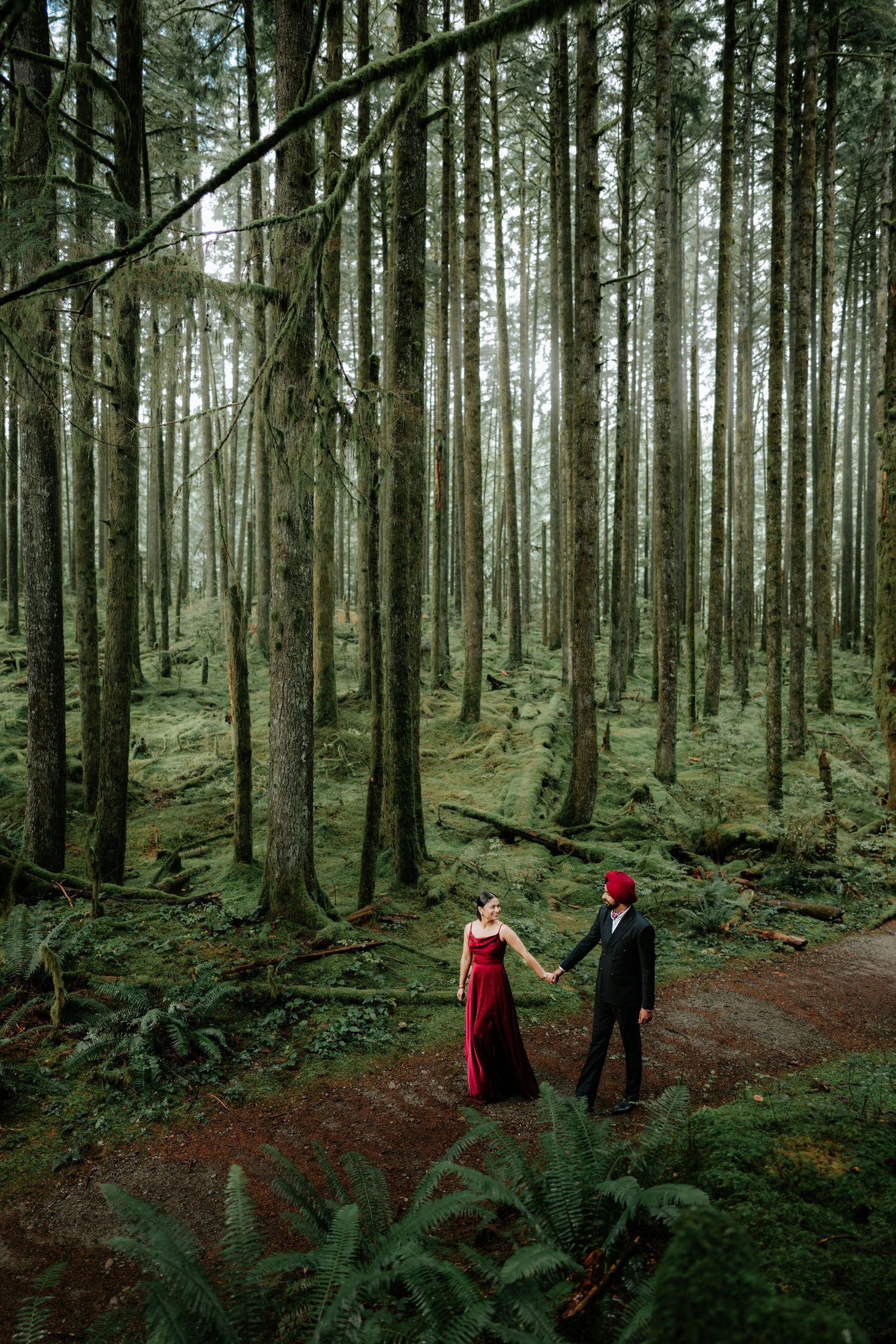 Two people hold hands while walking through a mystical evergreen forest.