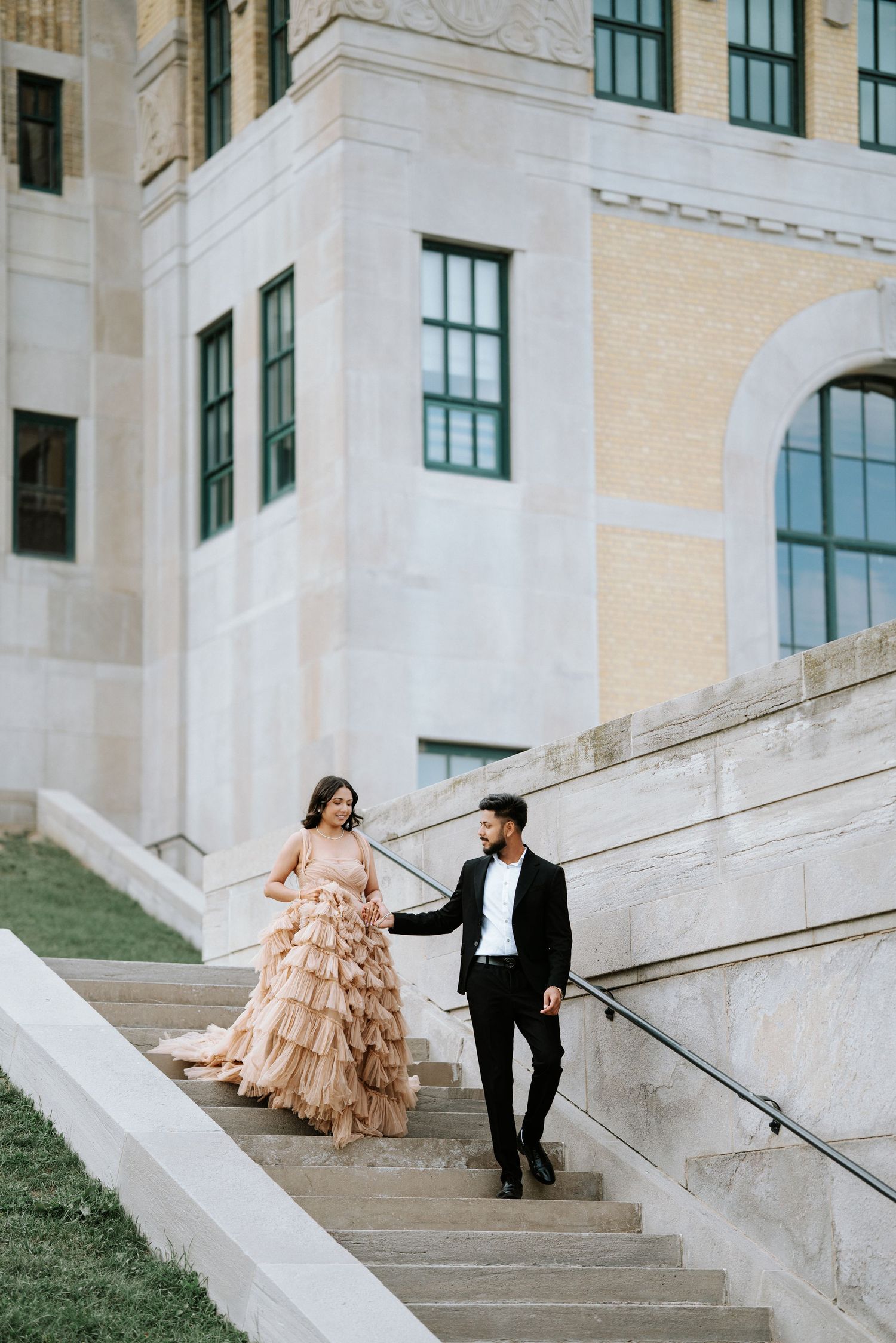 Couple in formal wear descending elegant stone steps of historic building.