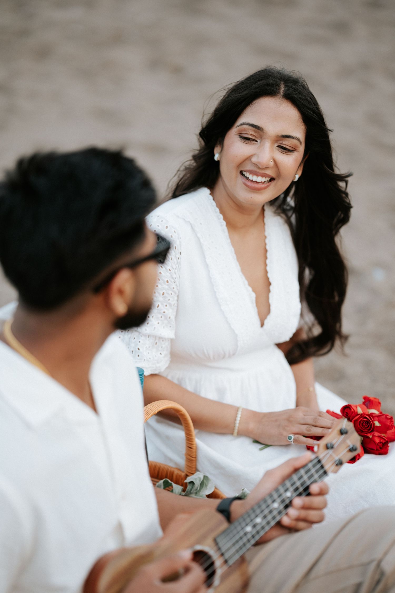 A romantic beach scene with a ukulele and red flowers.