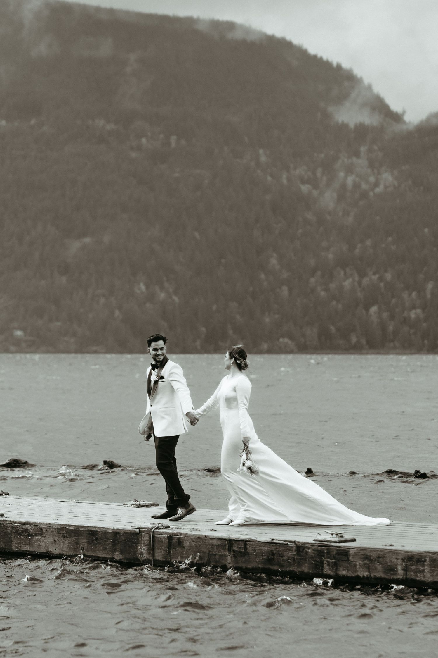 A series of four black and white photos showing a couple on a dock by a lake with mountains in the background.