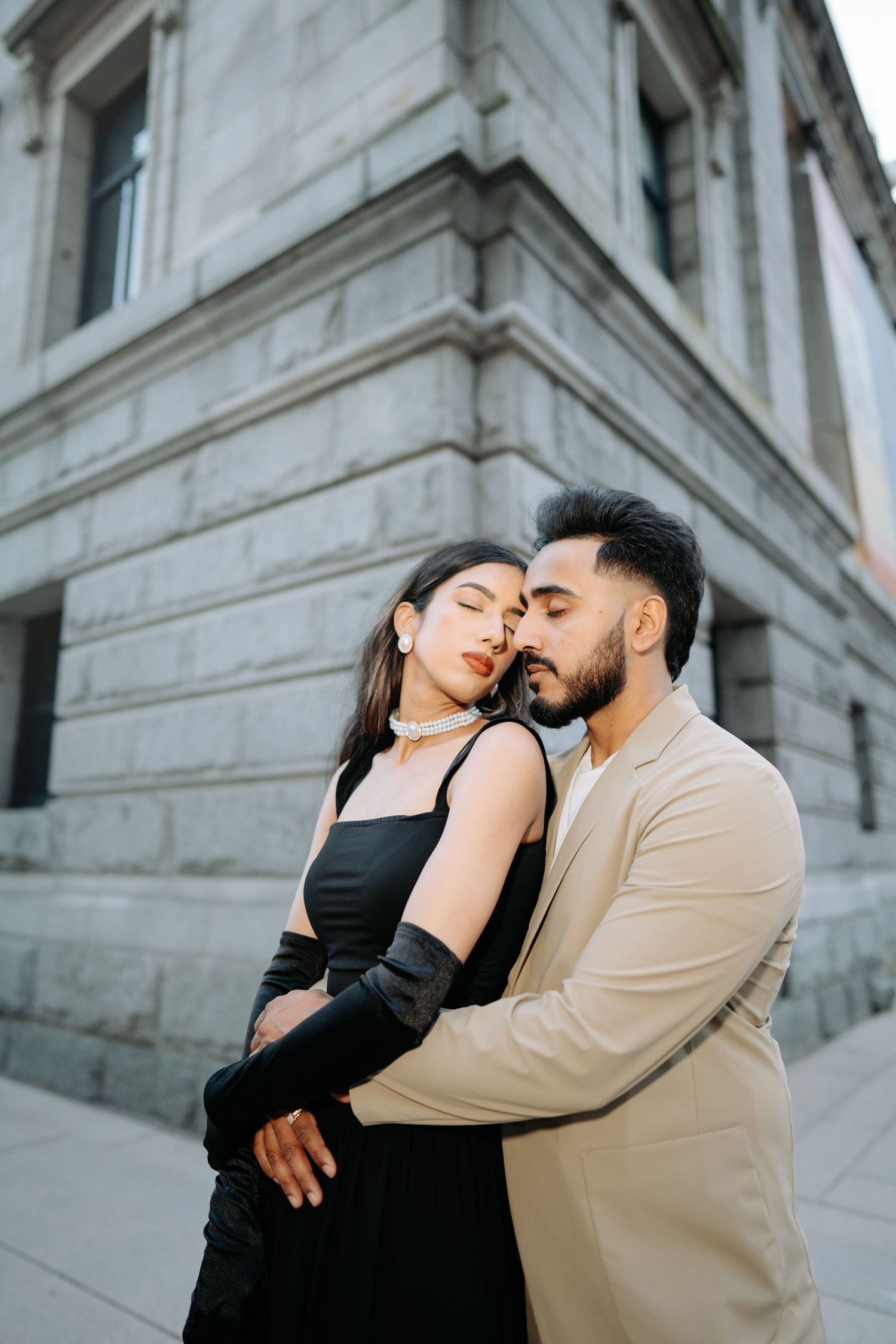 A romantic couple shares tender moments in front of a classic stone building with architectural columns.