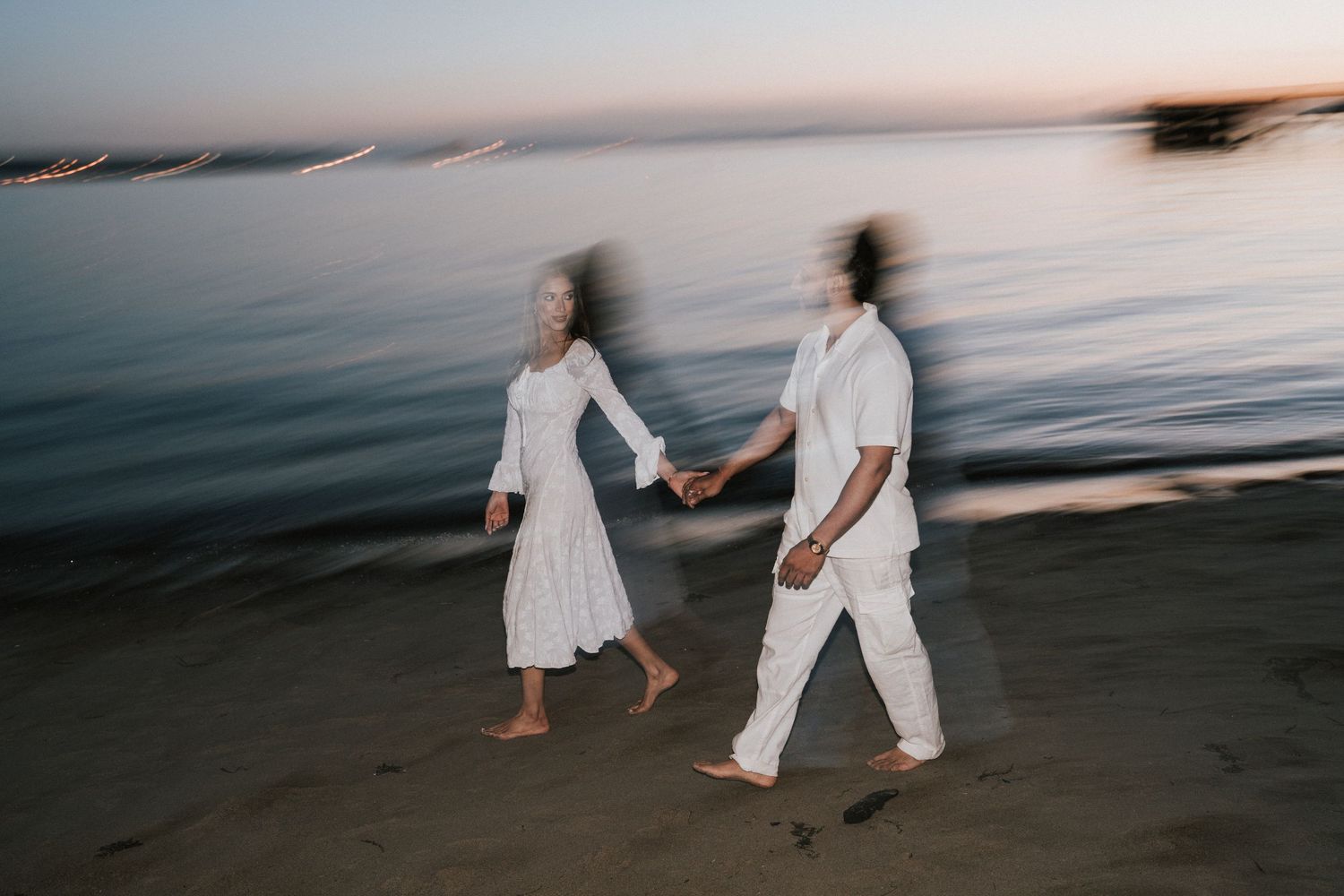 People in white clothing walking along a scenic beach at sunset creating a romantic silhouette against the ocean.