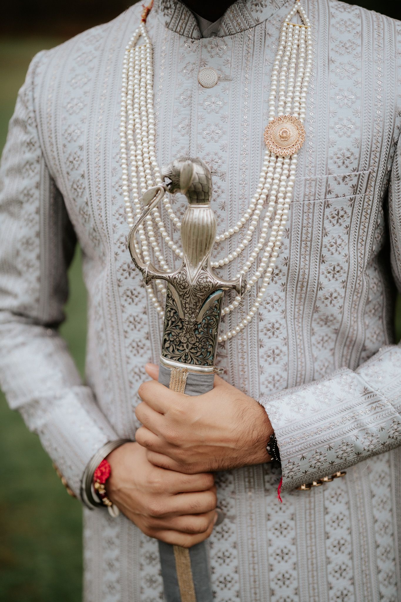 Groom wearing traditional white embroidered sherwani with pearl necklace and silver accessories.