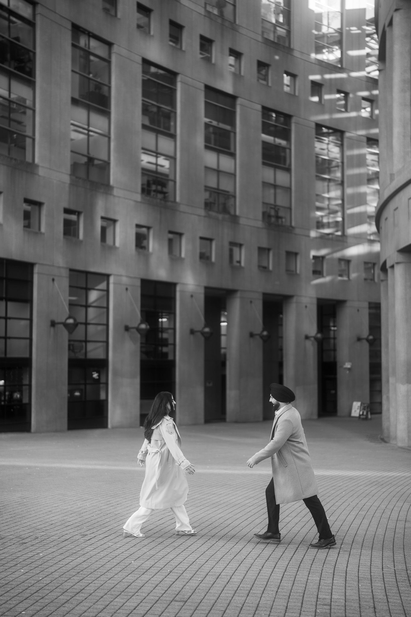 Black and white photo sequence showing two people walking across a modern urban courtyard with tall columns and glass walls.