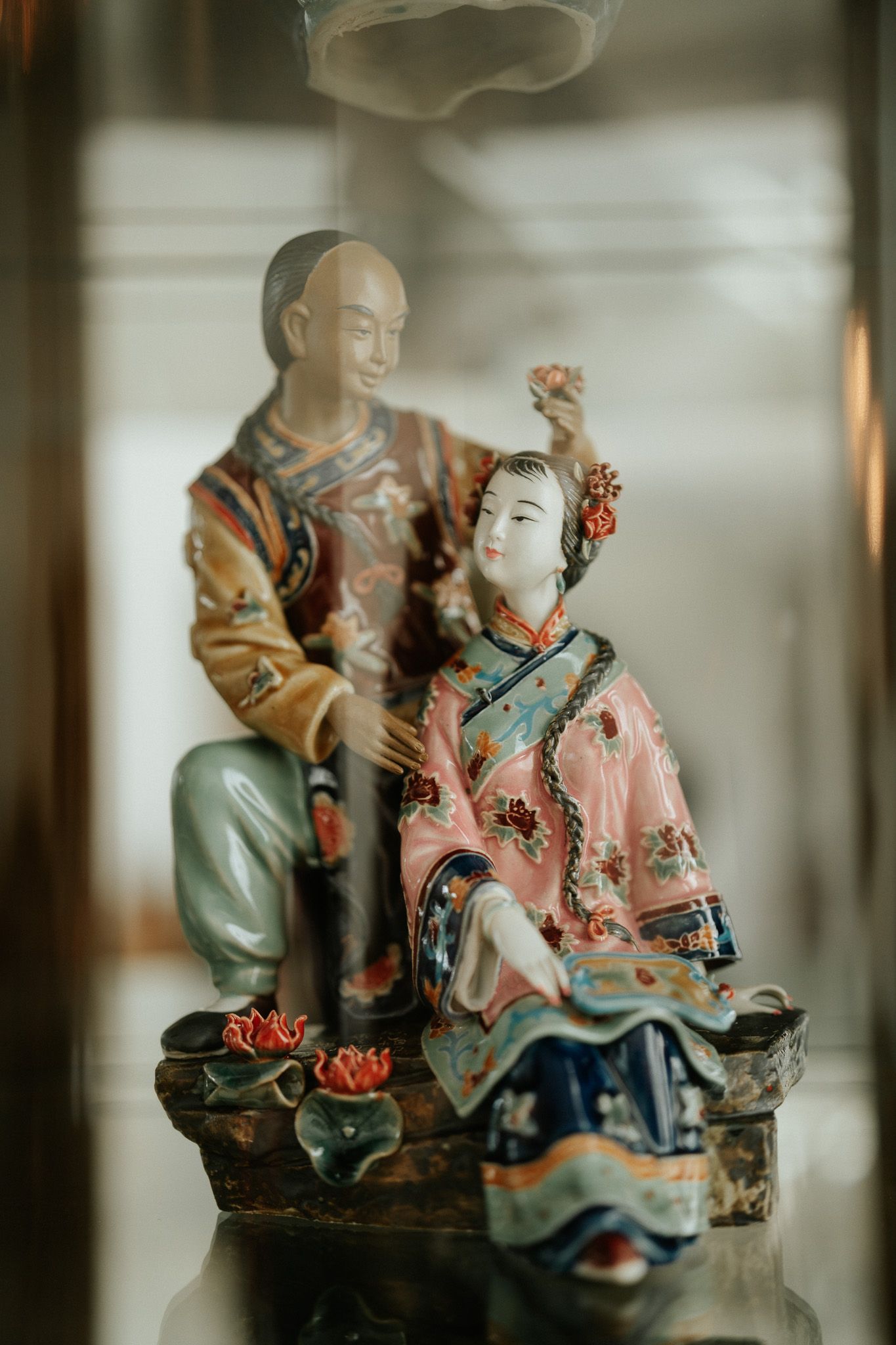 Colorful Chinese porcelain figurines of a man and woman in traditional attire displayed behind glass.